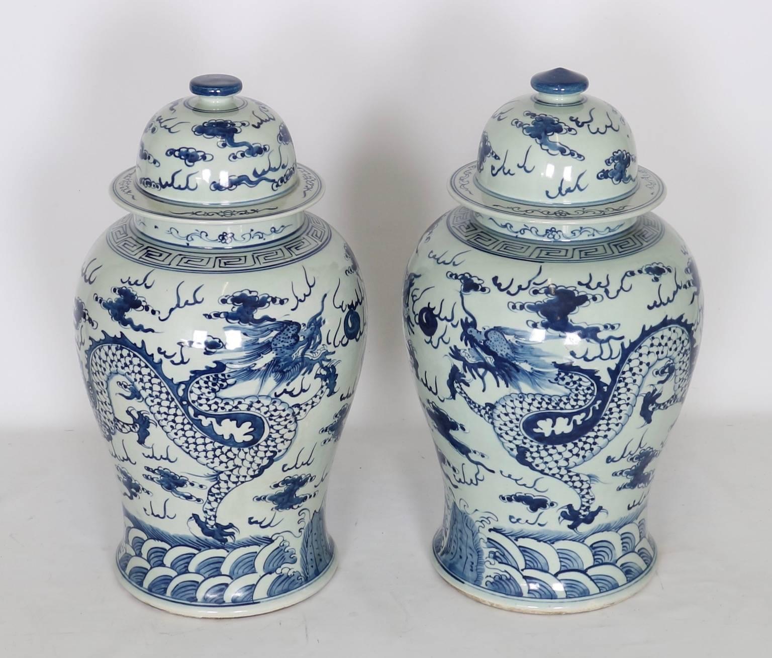 Chinese export ginger jars dating from the late 20th century. Features blue illustration against a white background of a pair of dragons above the sea. The pair include matching lids. Wear consistent with age and use. The pair are in excellent