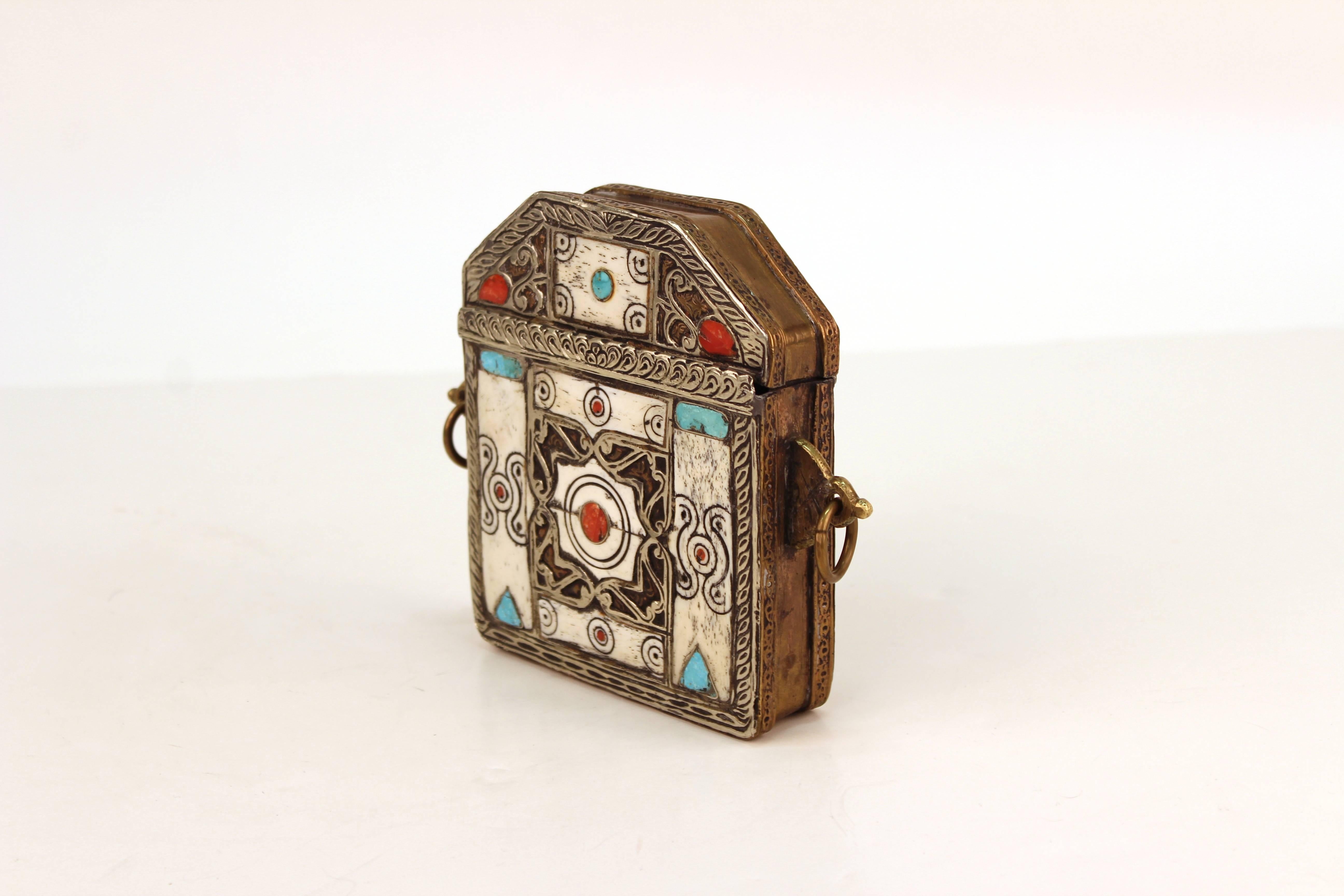 Koran box likely from North Africa. Crafted in mixed metal with brass and silver tones. Decorated with bone, coral and turquoise. Wear appropriate to use and material. The piece is in good condition.