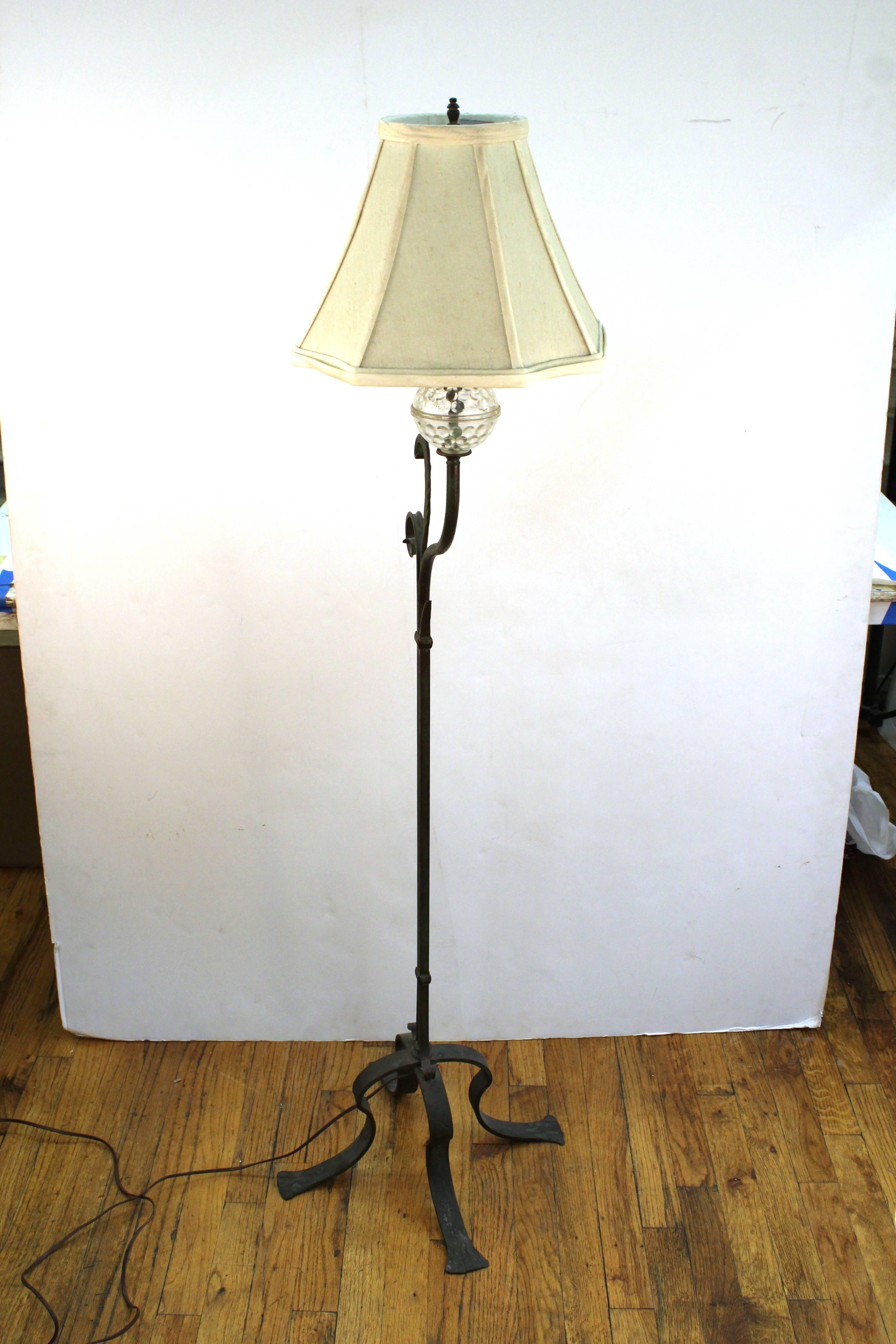 A wrought iron standing floor lamp with swag detailing and a cut-glass sphere. In good vintage condition.