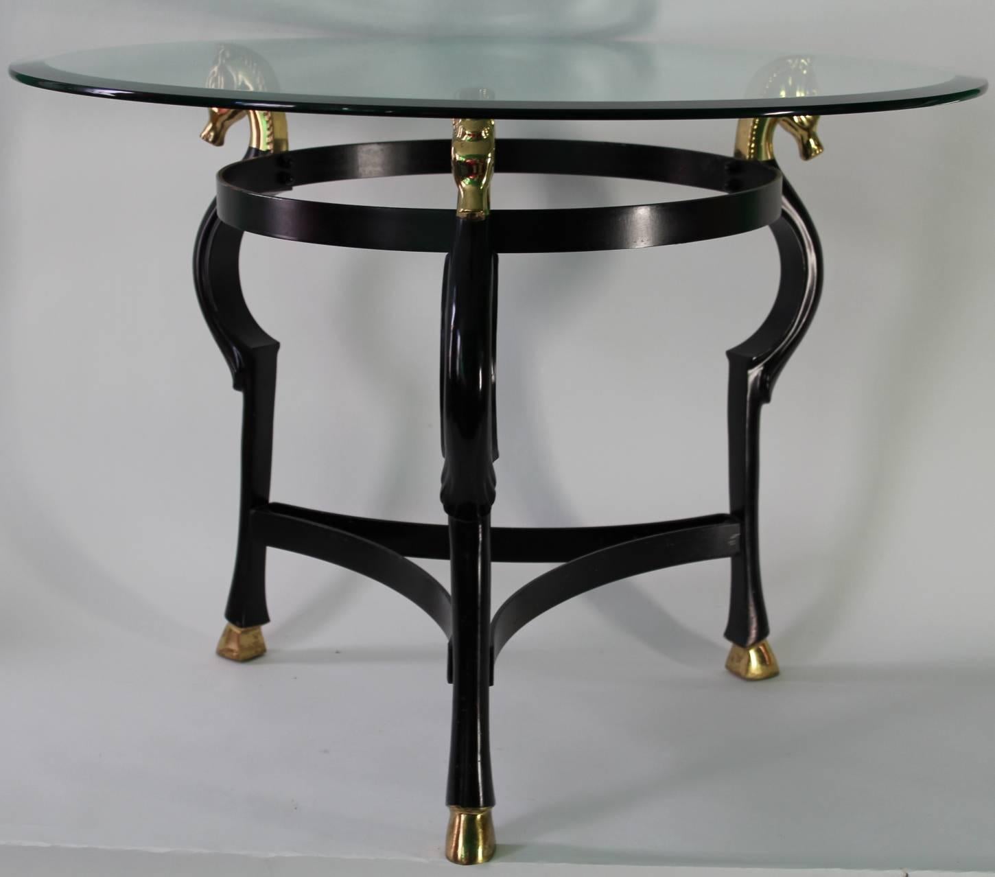 A Mid-Century Modern round end or side table in ebonized brass with seahorse heads and hooves motif and a circular glass top. The piece was made in the 1970s in Italy and is in good vintage condition.