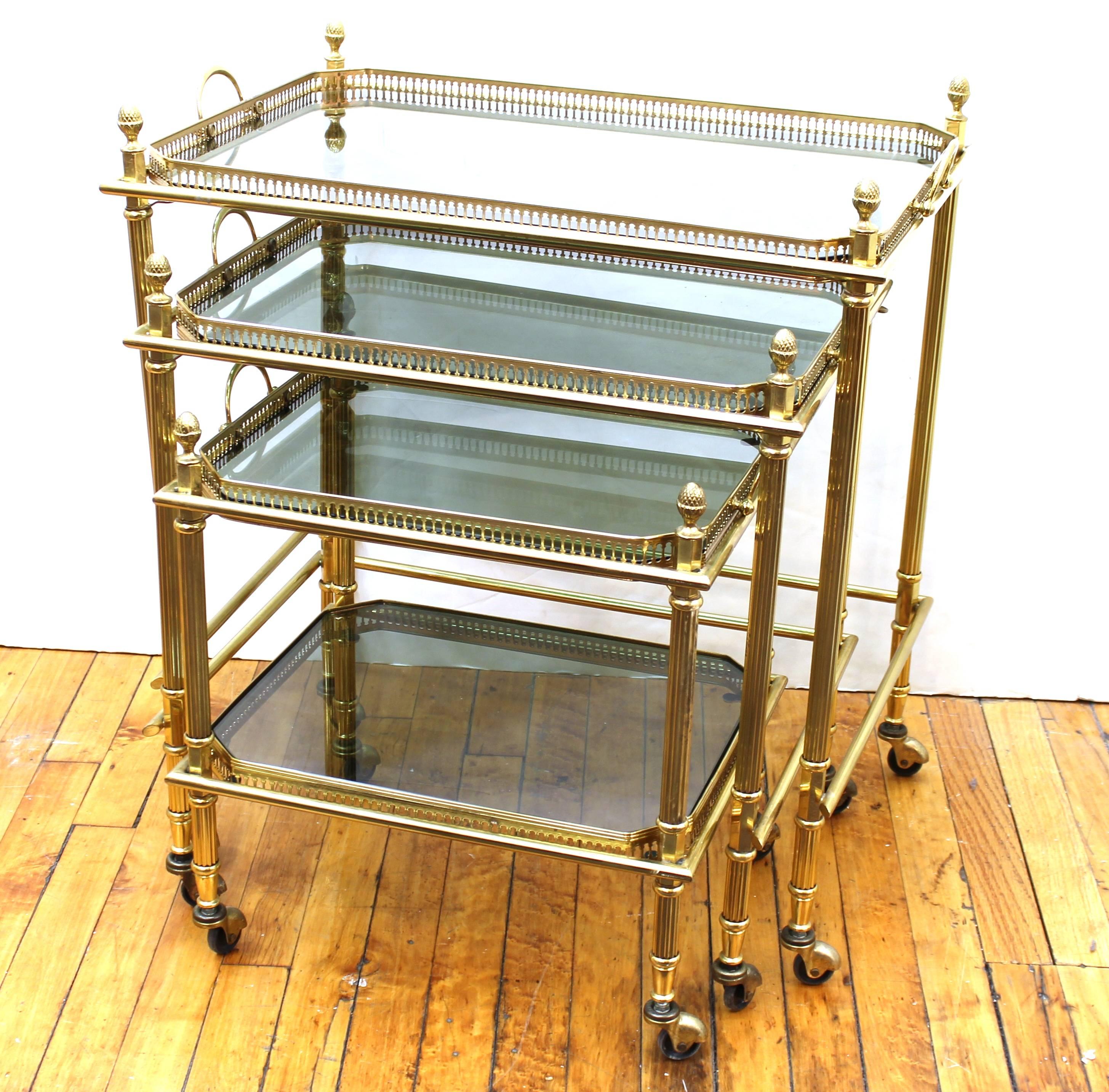 Maison Baguès nesting tables from the mid-20th century on casters. Featuring polished brass frames, and fluted legs. The set includes four removable smoked glass trays with galleries. Some worn spots to brass on legs and caster caps. The set remains