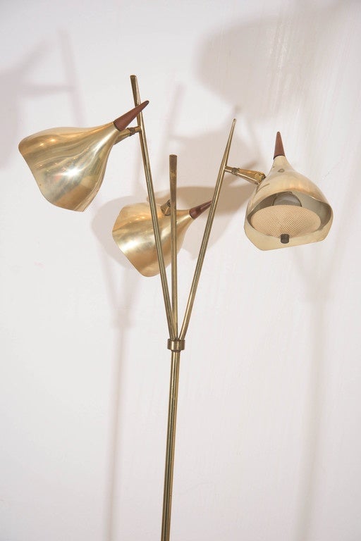 A vintage Italian three-light floor lamp, produced Midcentury in the style of Stilnovo, with adjustable tulip light shades in brass, each with perforated metal diffusers and pointed wood finials, affixed to brass stem, on a circular wooden base.