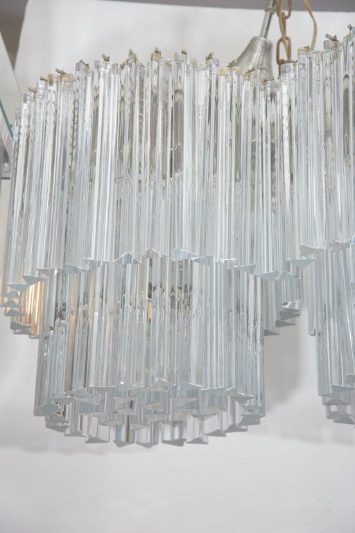 A vintage double chandelier, produced Midcentury by Venini, with two tiers of suspended glass triedri prisms, against a metal frame, height from tapered canopy is adjustable. Requires eight candelabra base bulbs. Good condition, with age appropriate