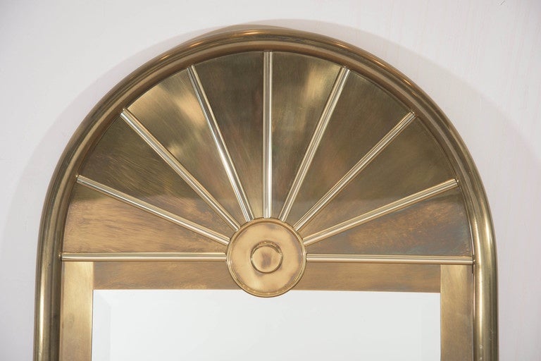 A massive arch form wall mirror, produced circa 1960s by Mastercraft, with brass frame, surmounted by stylistic fan design, and inset with beveled mirror rectangular mirror. Markings include maker's label [Mastercraft], fixed to the lower left