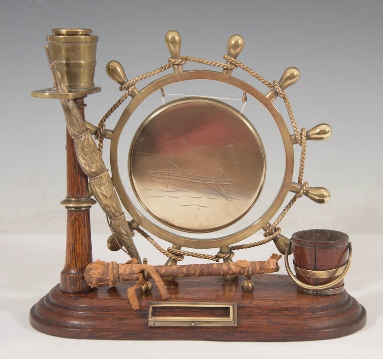 An English, antique dinner gong, striker included, designed with a nautical theme, created during the Victorian period, circa 1890s; the brass gong, with engravings depicting two rowers, hangs suspended from a brass ship wheel, wrapped in highly