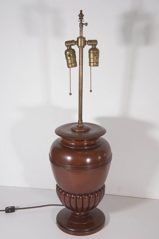 A vintage, highly unique table lamp, including double cluster sockets on long brass stems (two pull chains included), above urn form, carved mahogany wood body, with gadrooned detailing above a circular base. Height is adjustable, ranging between