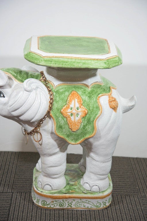 A vintage, ceramic elephant garden seat with raised trunk, produced circa 1960s-1970s, hand-painted in green and gold tones, with metal necklace. Good condition with age appropriate wear, slight chip to the base.