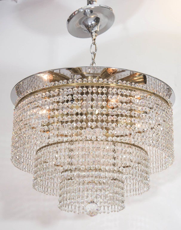 A vintage waterfall semi-flush mount chandelier, produced in Italy, circa 1950s, with hanging Swarovski crystal beads and single cut drop, suspended from three tiers of circular brass frames, descending from largest to smallest, affixed to the