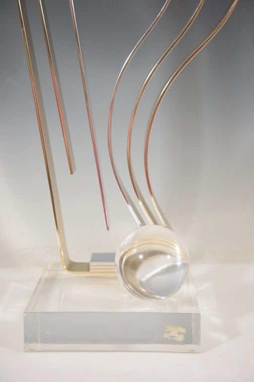 A vintage, Kinetic sculpture by artist Dan Murphy, circa 1980s, with beautifully polished sheets in brass, and a single chrome, manipulated into the form of an abstract flame, above a Lucite base, with accent sphere. Markings include the artist's
