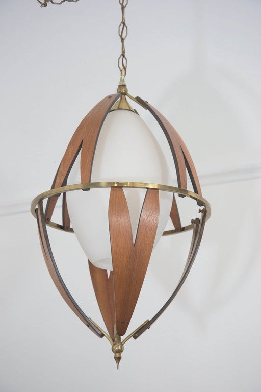 A vintage Scandinavian pendant, produced circa 1960s, with egg form milk glass shade, surrounded by brass frame and ring, with curved, petal form slats of teakwood, top and bottom surmounted by brass bulb finials; approximately 100