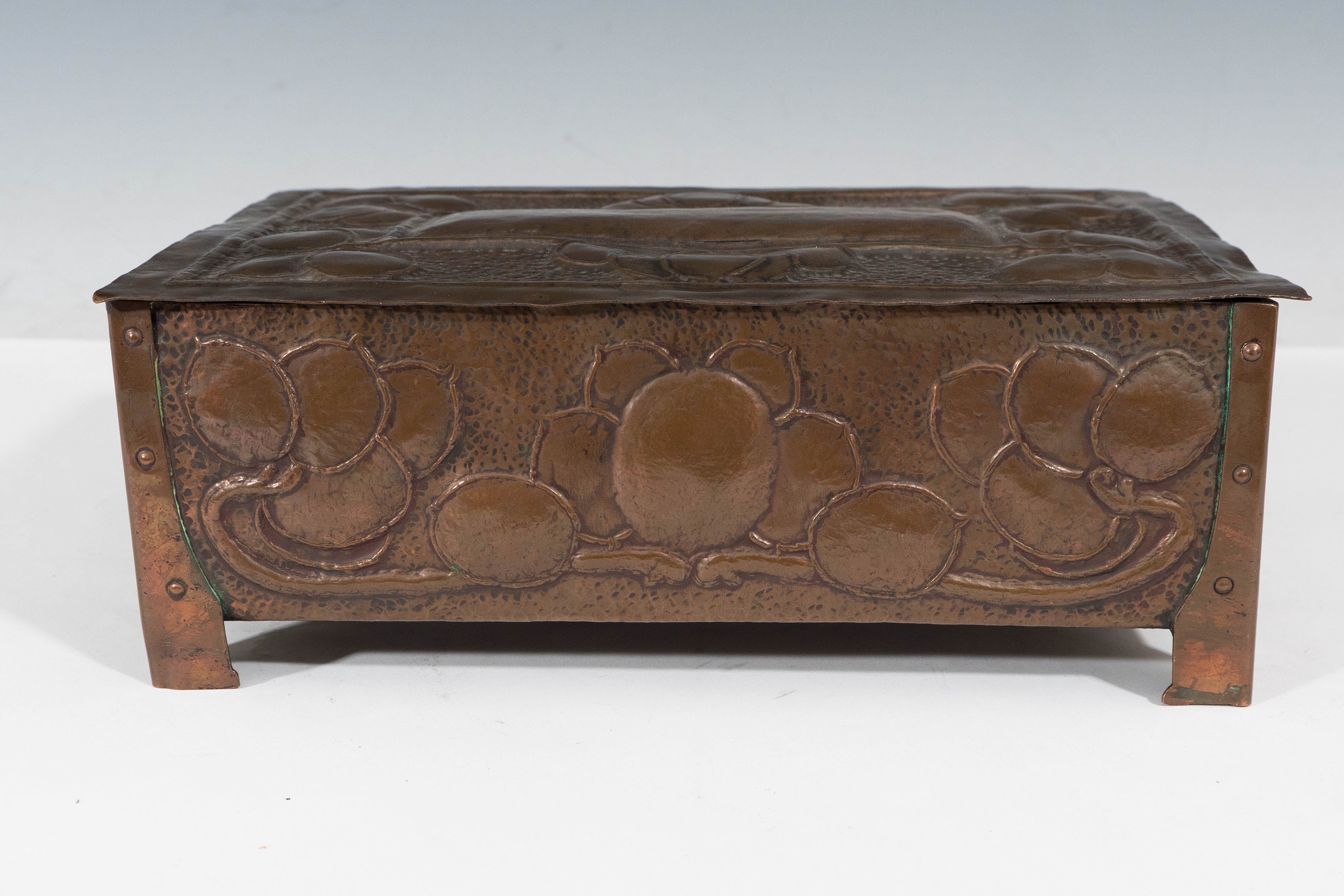 A vintage English copper box, produced within the Arts & Crafts movement, circa early 20th century, decorated to all sides with repousse details of fruit and curling vines, against a hammered ground; interior lined with gold colored velvet. Good