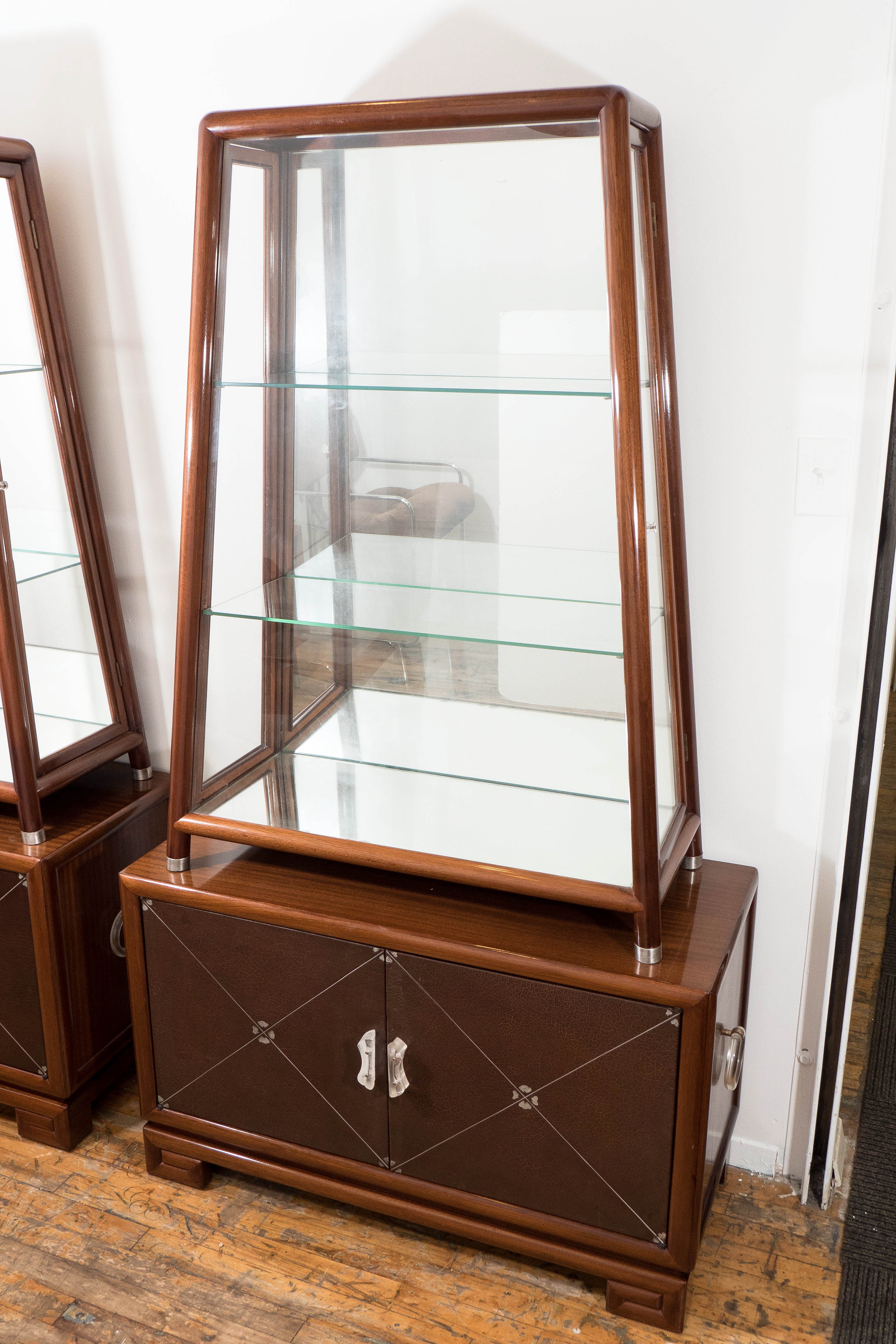 Art Deco cabinet produced circa 1940s by Grosfeld House, in polished mahogany wood. The top part includes adjacent wood framed glass doors and lucite pulls, with glass shelves and mirror panels to the bottom and back, resting on brushed metal feet.