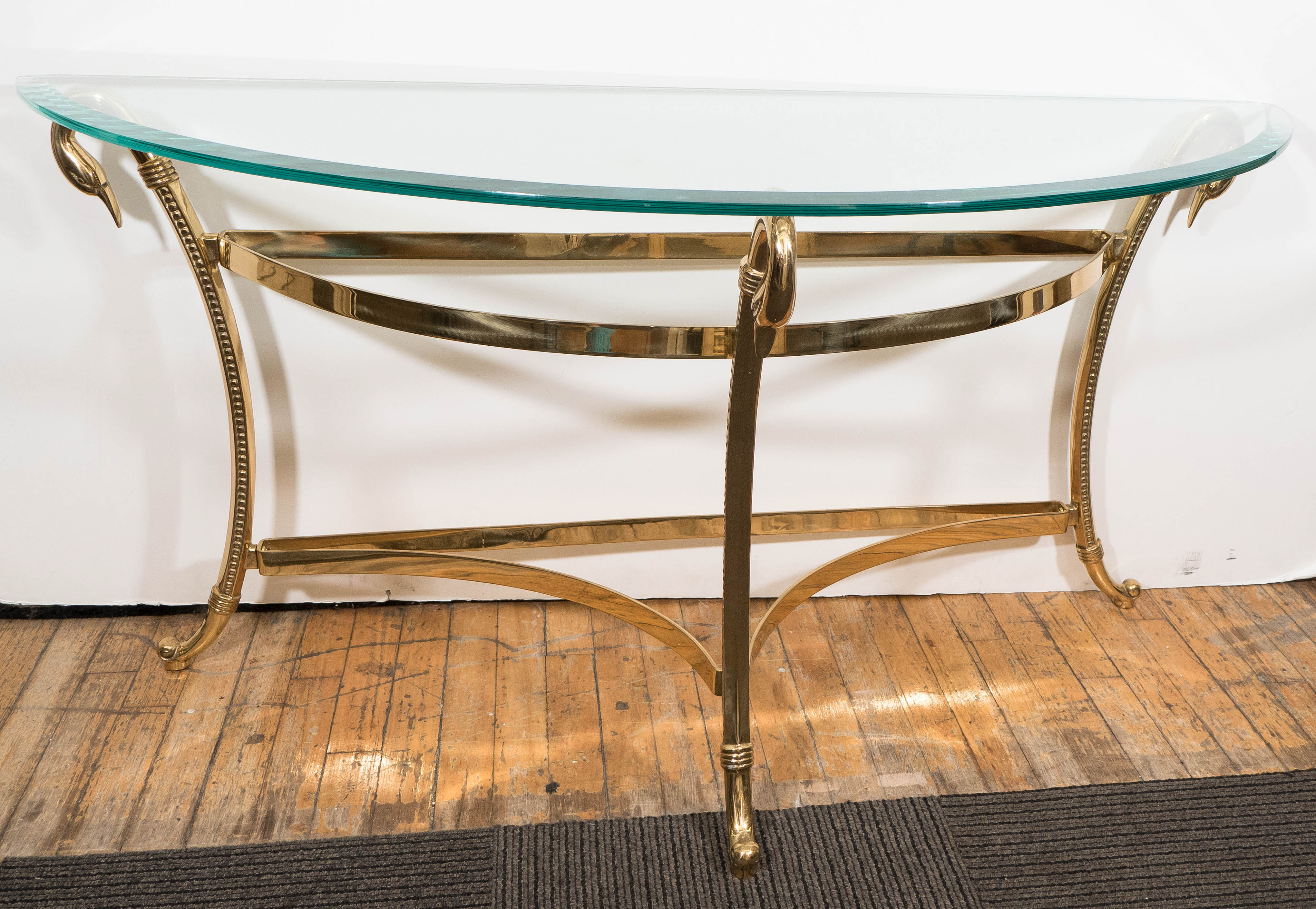 A vintage demi-lune, Hollywood Regency style console table, produced circa 1970s, with beveled glass top on polished brass frame, with three supports, each with swan head motif, over two stretchers, terminating on curved legs. Very good condition,