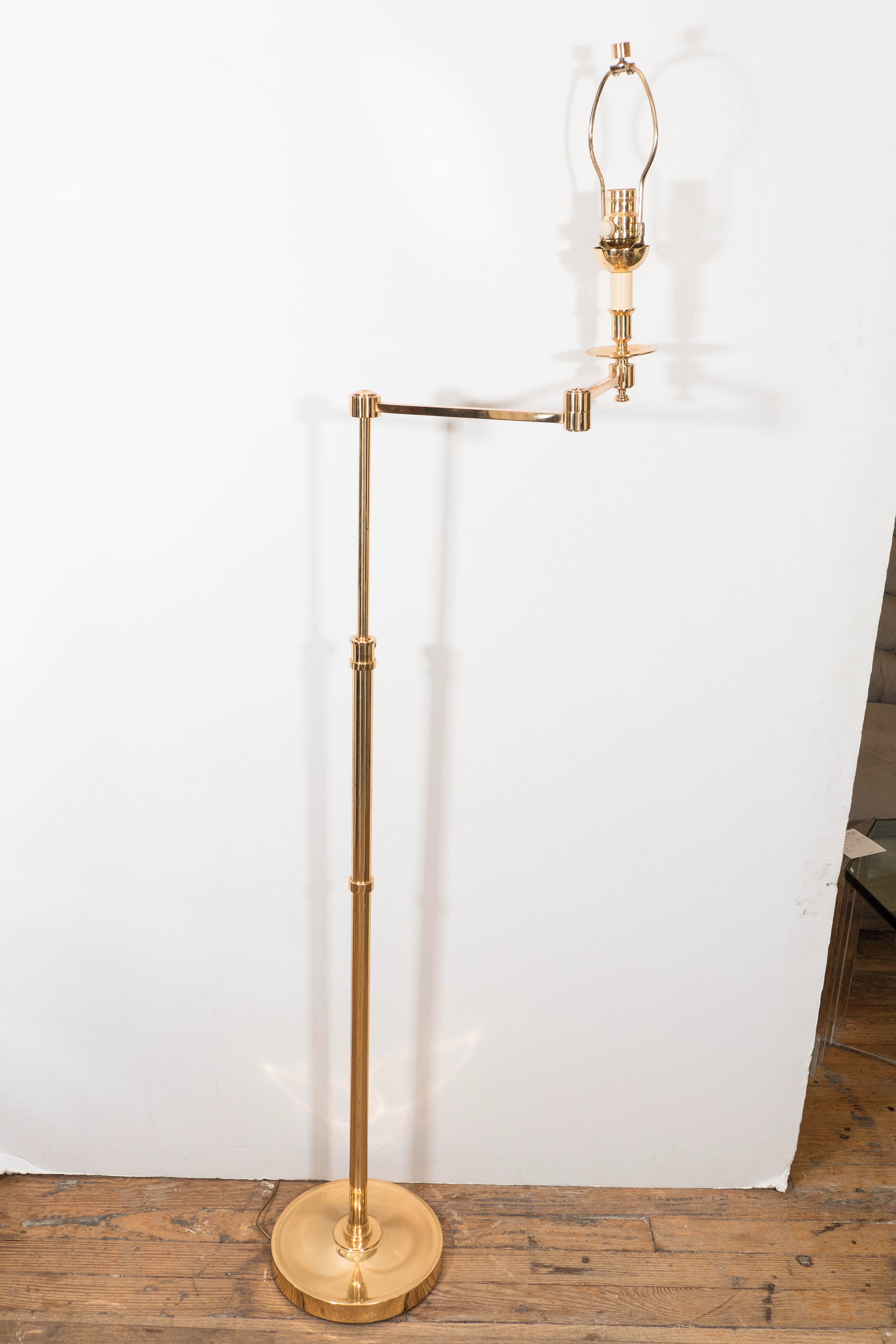A beautifully polished brass floor lamp, with single socket and decorative bobeche, supported by a Nessen style articulated arm, over an adjustable stem on a circular base; harp and finial included. Wiring and socket to US standard, requires a