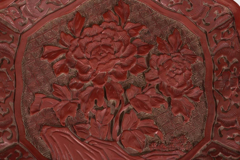An antique, Chinese carved cinnabar plate, produced circa 1750-1800s, with raised and curved hexagonal edge, surrounding an ornately detailed pair of blossoming flowers. Very good antique condition, consistent with age and use.