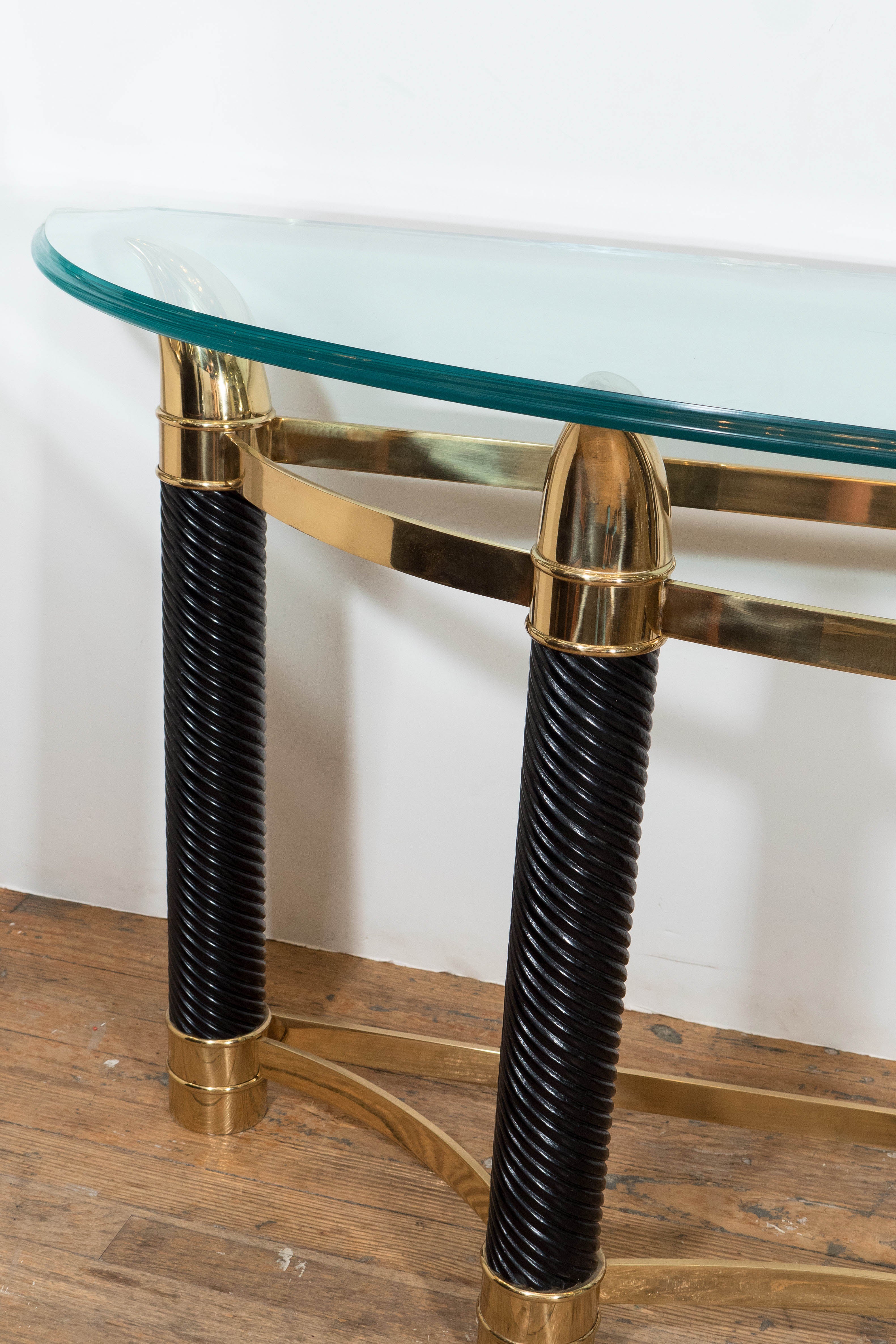 An Italian vintage Mezza Luna Italian console table, which features beveled glass top, on turned wooden legs, finished with polished, gold-toned brass ‘horns,’ and two brass stretchers. Good vintage condition, consistent with age and use; the glass