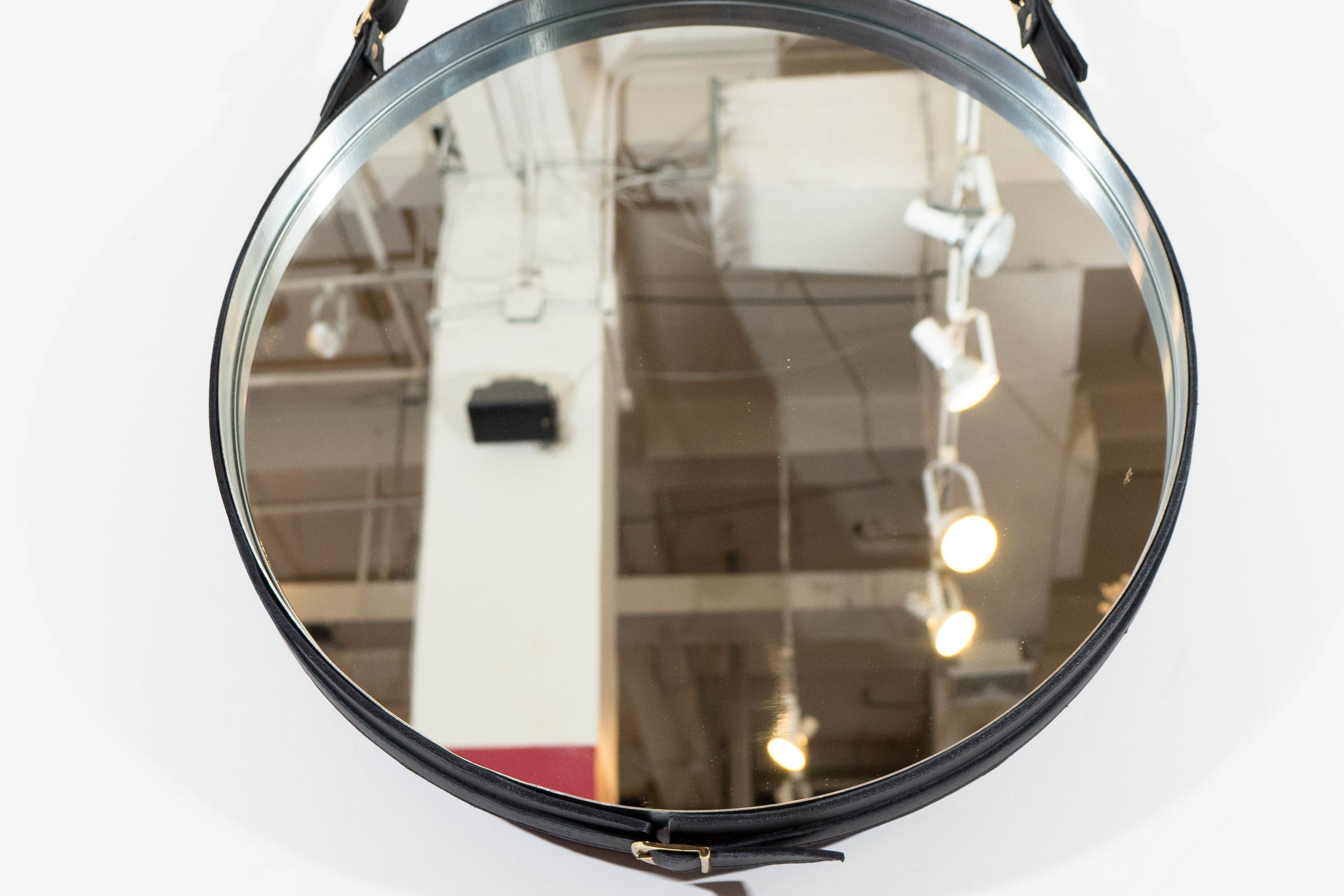 A round Adnet wall mirror, based on the original design by namesake Jacques Adnet, the frame and strap-work in black leather, with brass buckles. Very good condition, consistent with age and use.