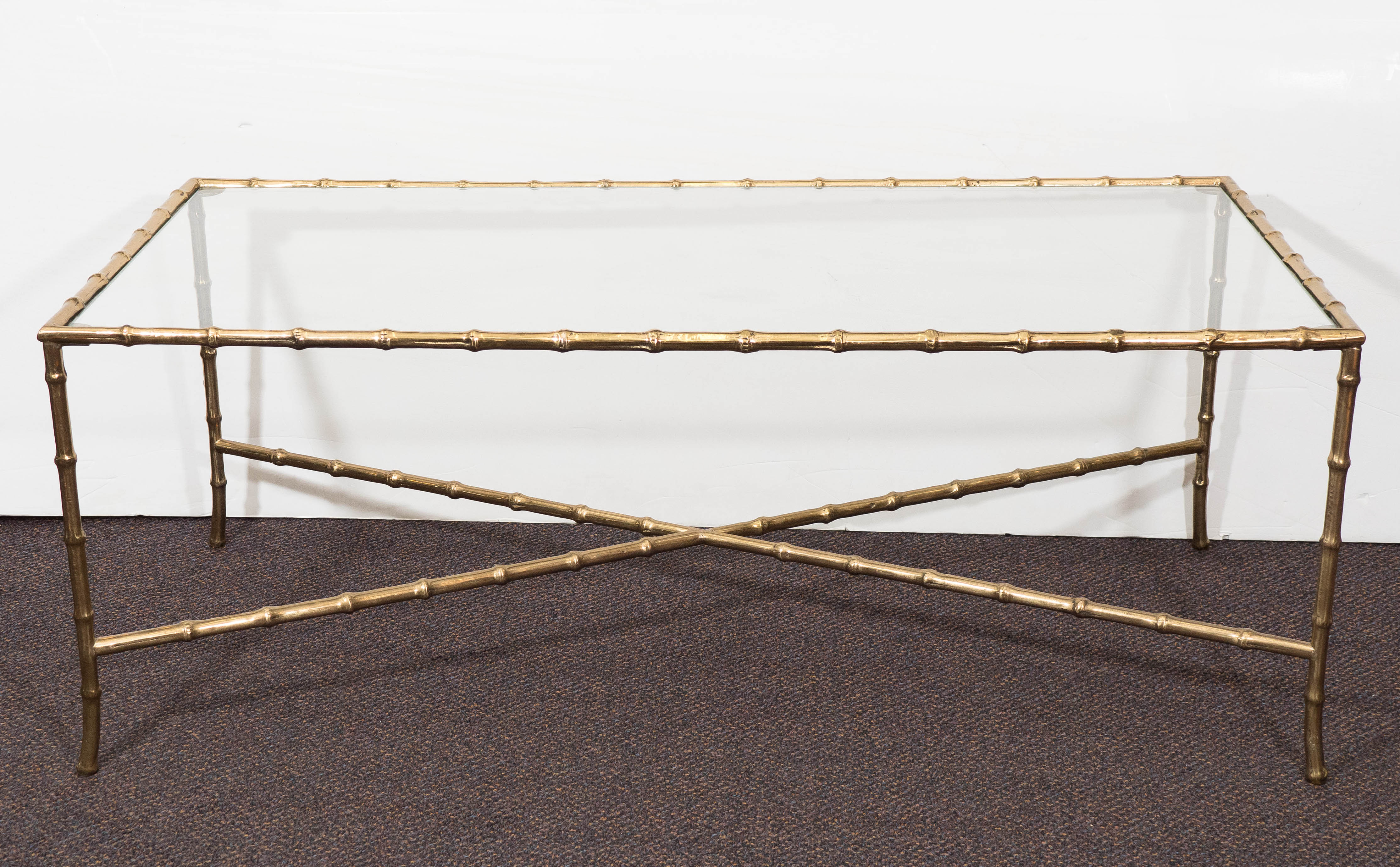 A vintage brass coffee table in the chinoiserie mode, produced circa 1960's by French designer Maison Baques, with glass top over faux bamboo frame and cross beam stretcher. Very good vintage condition, with minimal wear.