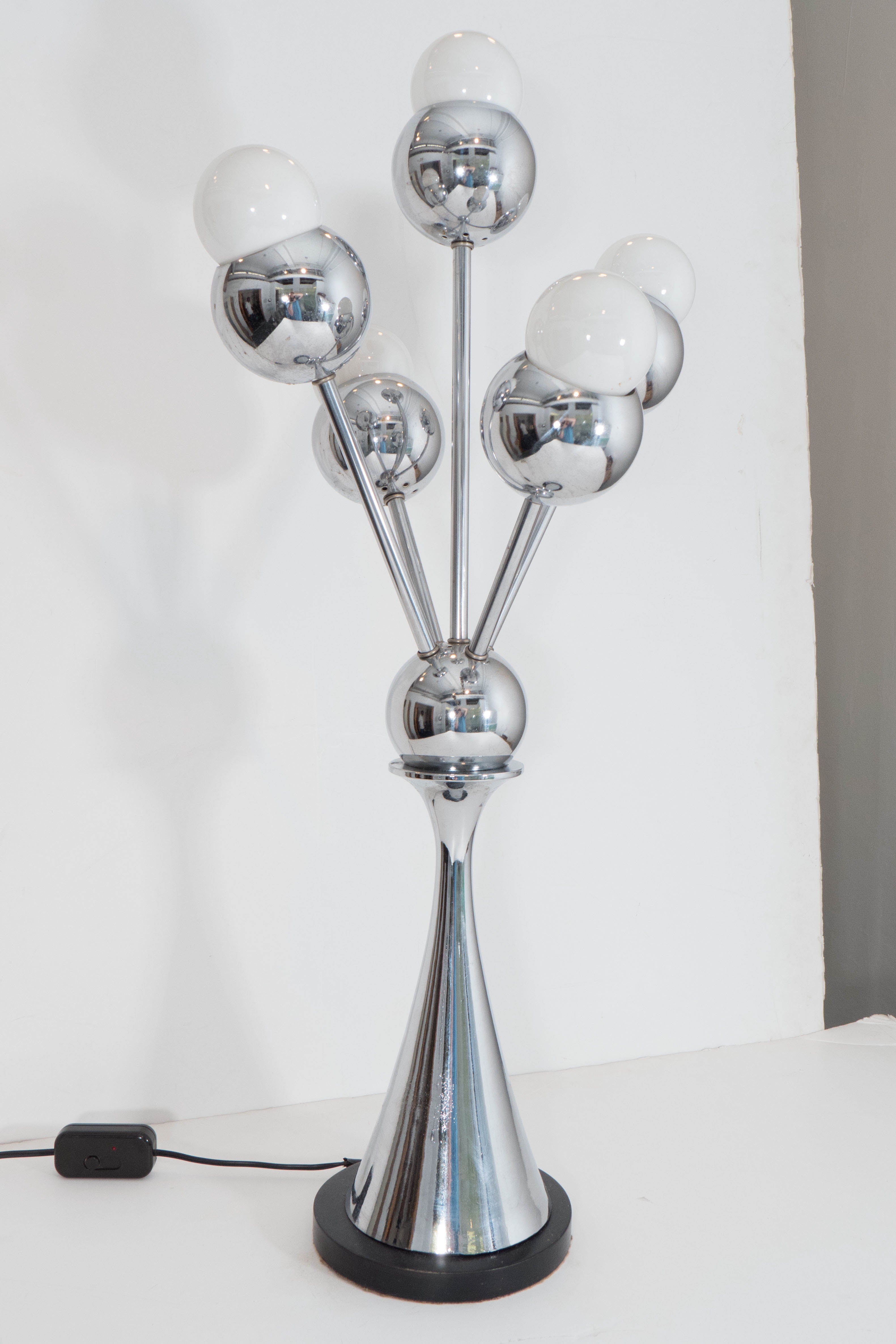 A pair of chrome table lamps, produced circa 1970s in the Space Age style, each with five globe form shades radiating from a nucleus, raised by a tapered shaft on a circular black painted wood base. Wiring and sockets to US standard, requires five