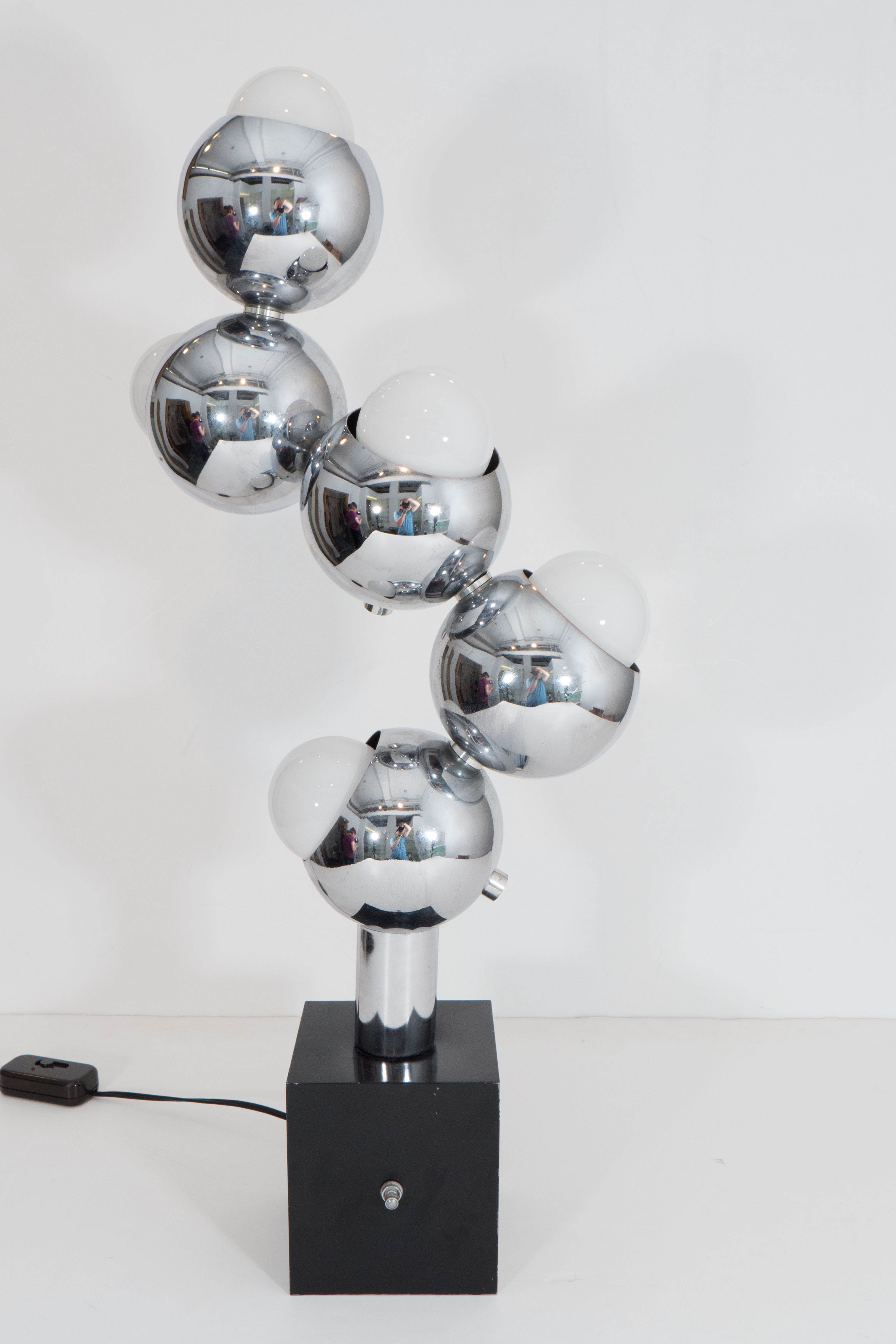 A highly unique 'Molecule' table lamp, produced circa 1960s in the style of designer Robert Sonneman, with five lights, each socket set within a round, polished chrome shade, clustered above a black enamel painted base. Wiring and sockets to US