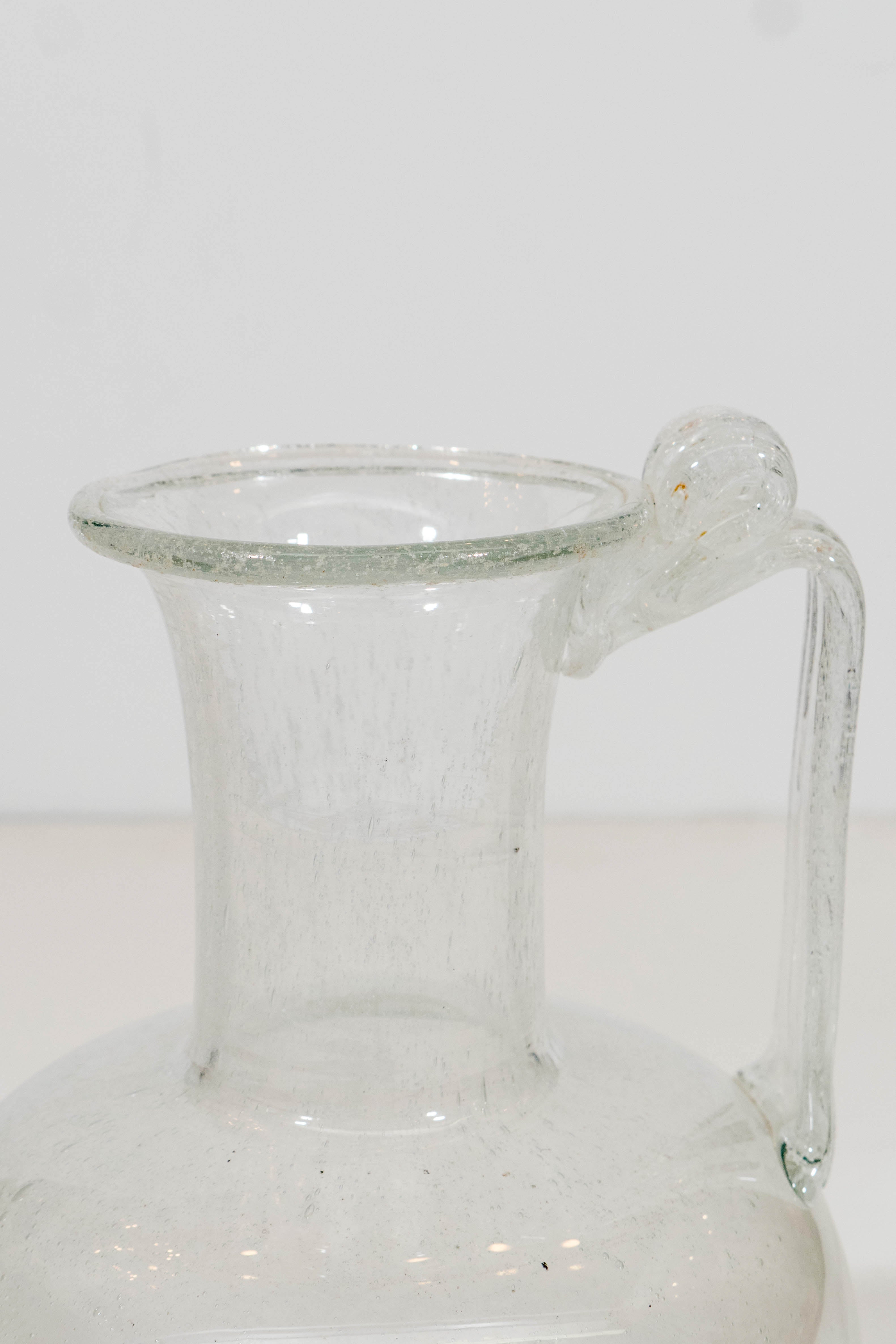 A vintage Venetian glass ewer or pitcher, features clear glass body with infused bubbles, and a handle that is finished with a decorative fold-over at the funnel mouth. Good vintage condition, with crackalure over the neck and handle.