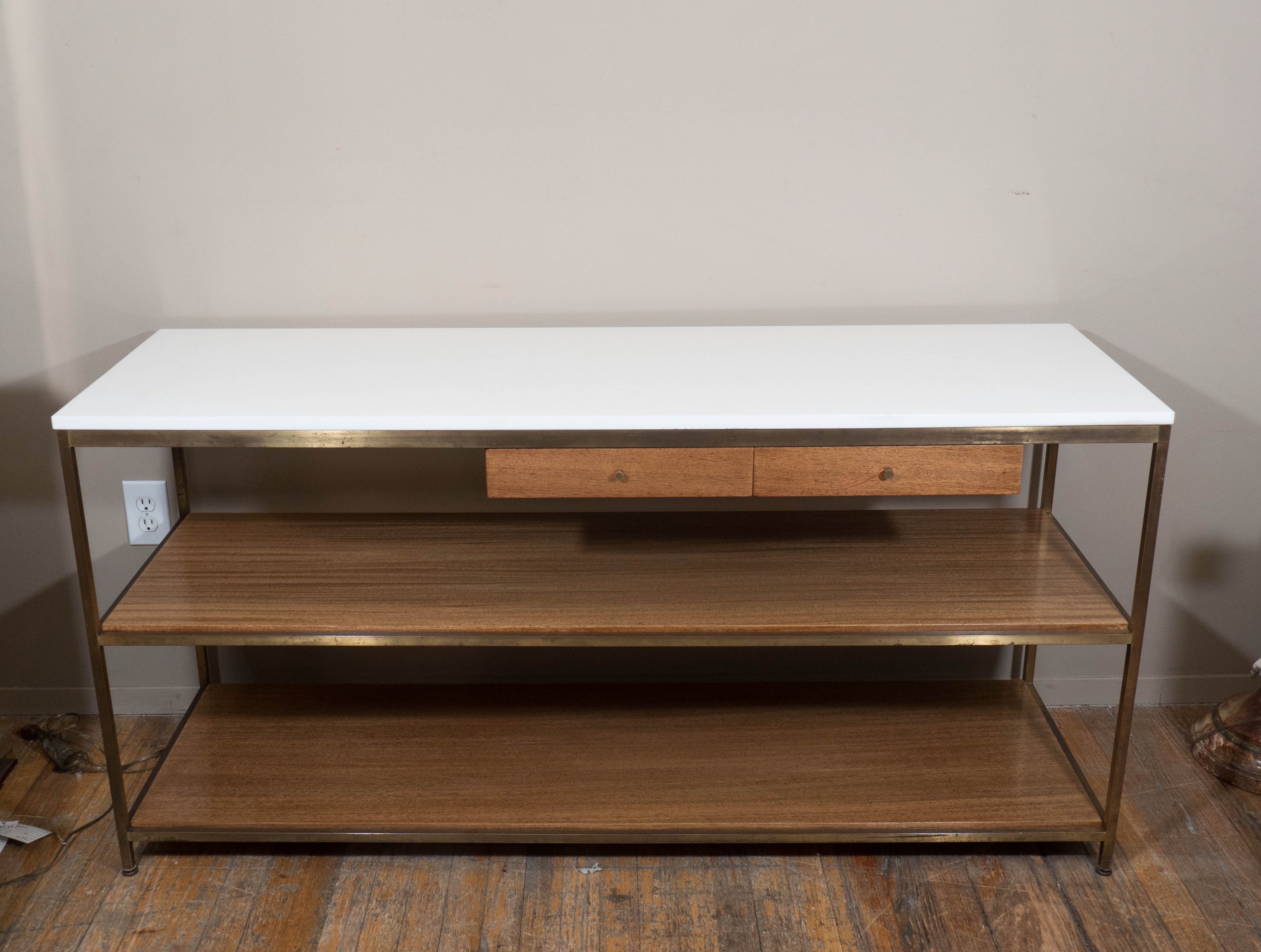 A vintage console, designed by Paul McCobb and produced circa 1950s by Calvin Furniture Co., with milk glass top on brass frame, with two exterior drawers, each with brass knob pulls, over two wood shelves. Markings include original label [Calvin,