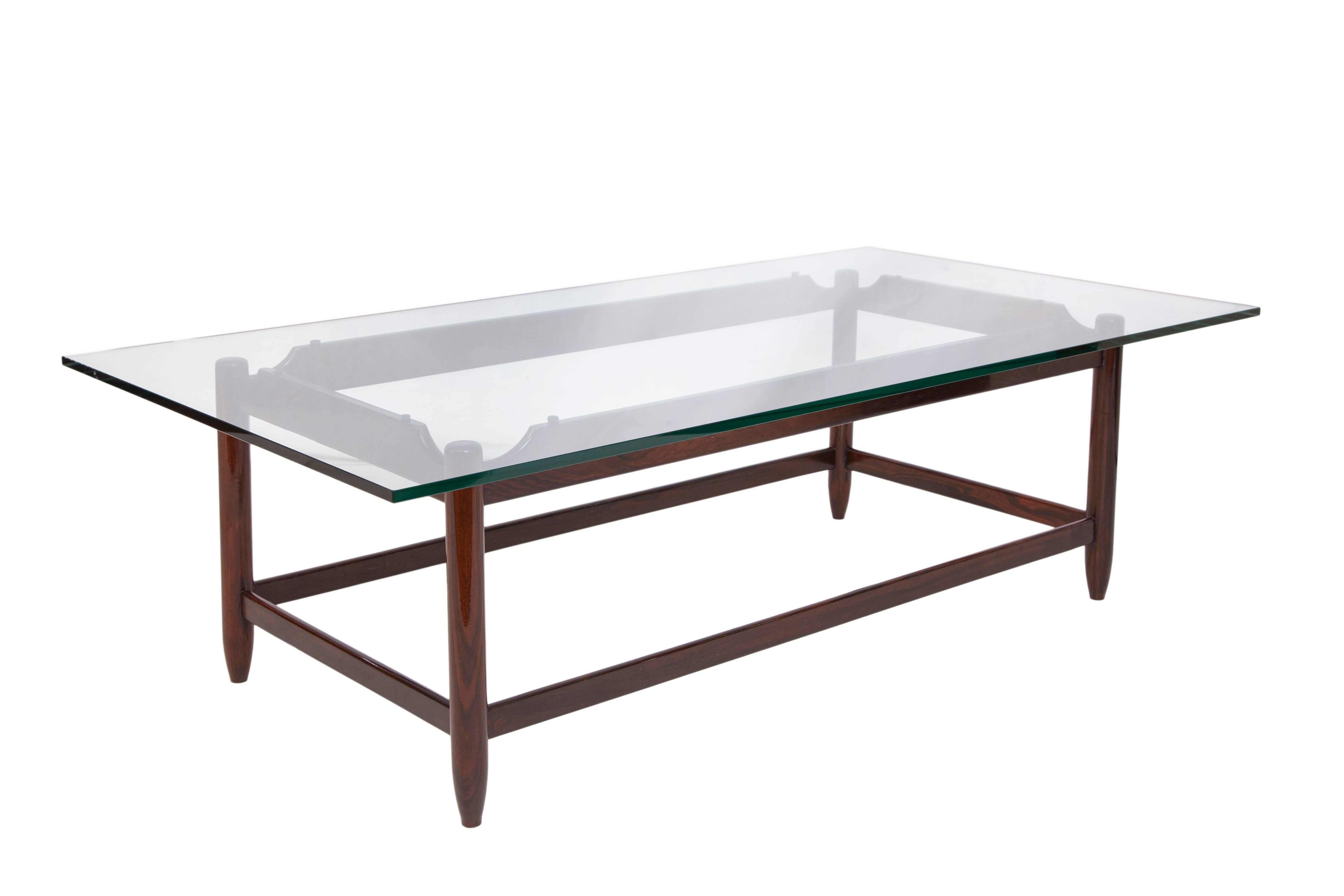A vintage highly modernistic glass top coffee table, produced circa 1960s by Brazilian architect and designer Sergio Rodrigues, on jacaranda wood base, with stretcher poles and tapered legs. Good vintage condition, consistent with age and use.