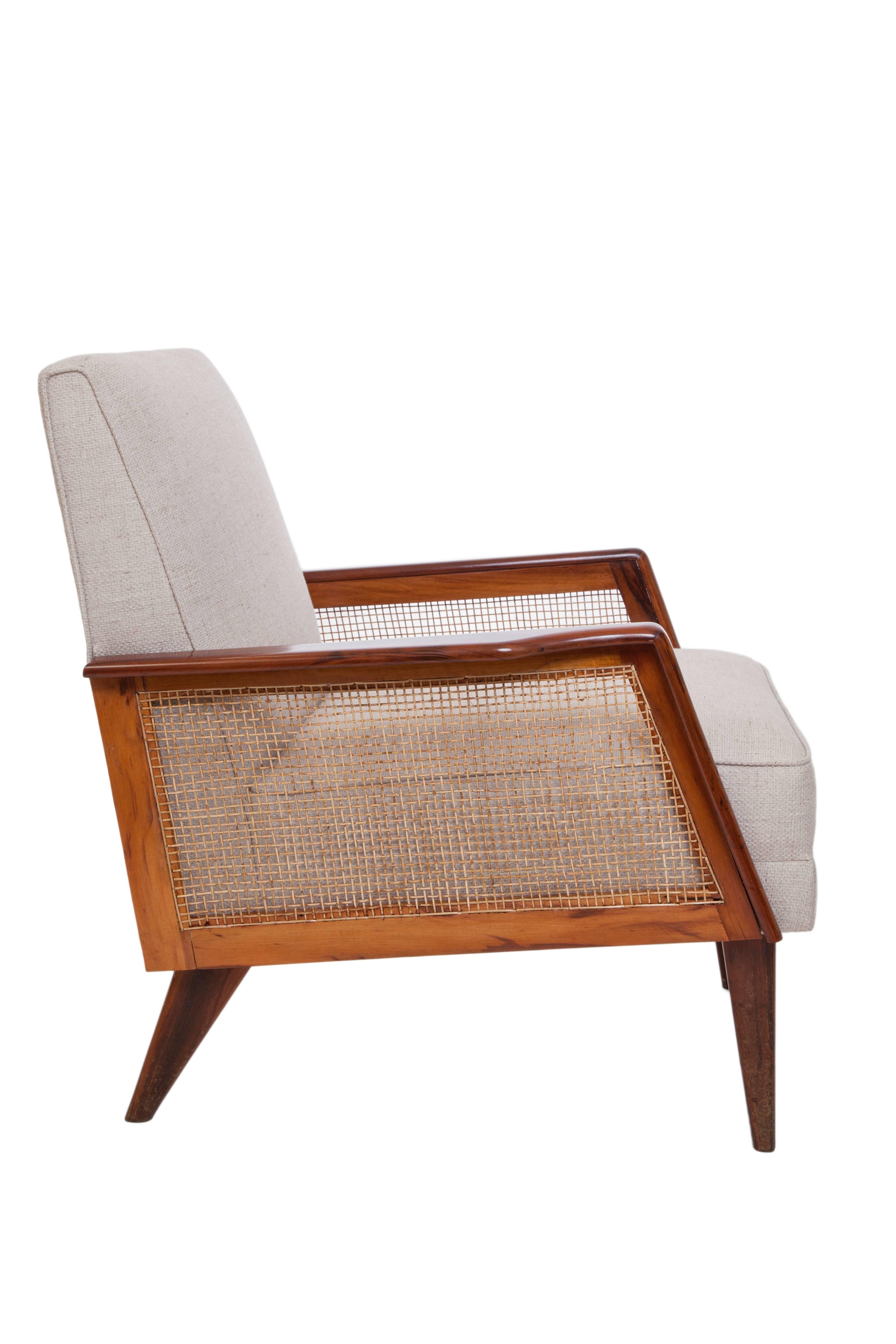 A vintage armchair, produced, circa 1950s, the cushioned back and seat upholstered in linen, with woven caned sides, against a beautiful Brazilian caviuna wood frame, on tapered legs. Very good vintage condition, with minimal age appropriate wear,