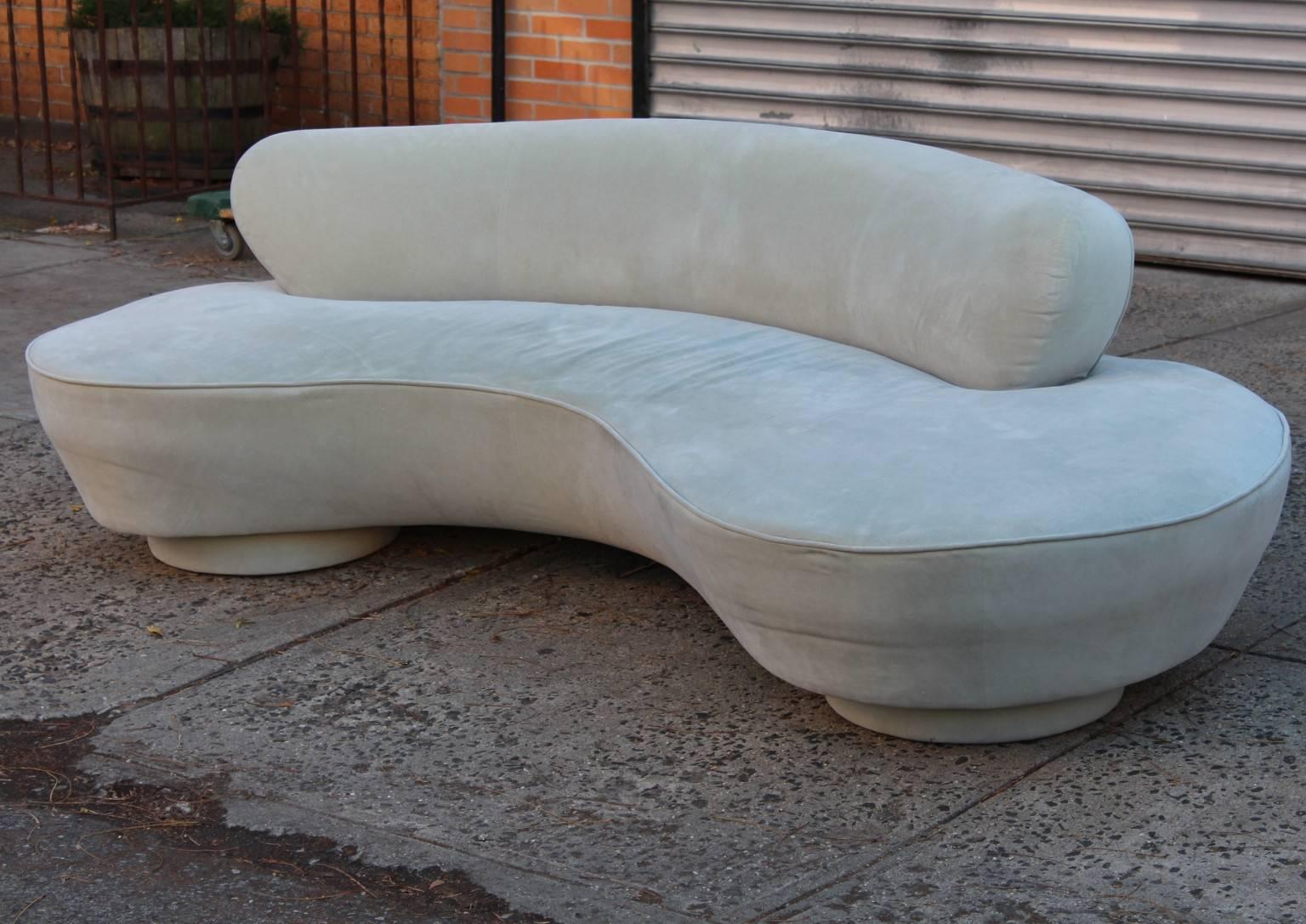This postmodern serpentine sofa, designed by Vladimir Kagan for Directional, circa 1990s, takes form as a curved seat with central backrest, entirely upholstered in light grey ultrasuede, with two rounded bases to each end and a middle Lucite
