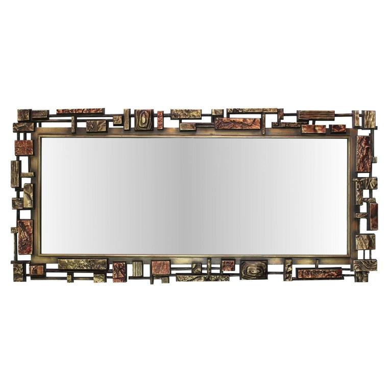A vintage, circa 1970s wall mirror, the glass inset within a Brutalist style frame in cast resin, with textured geometric shapes of varying sizes and metallic tones. Very good condition, consistent with age and use.

9449