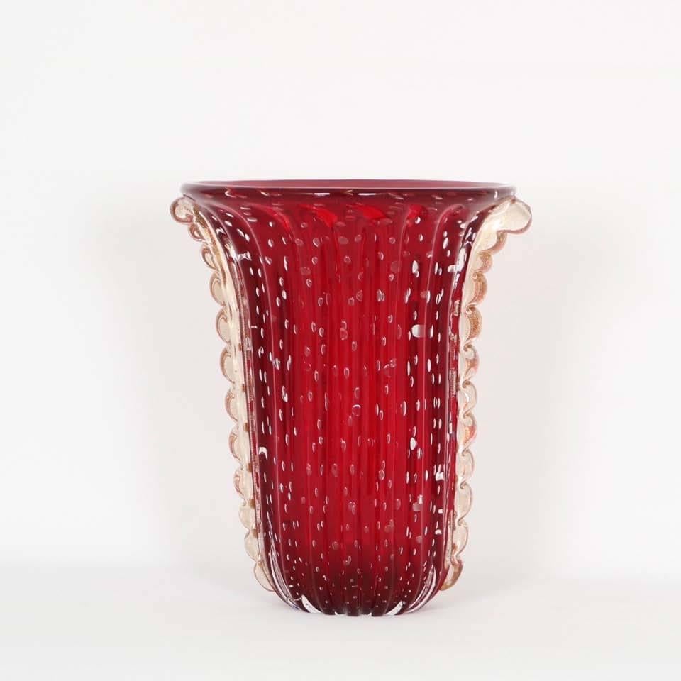 A vintage Murano glass ribbed vase, produced circa 1950s by Barovier e Toso, in vibrant cranberry color, decorated with bullicante bubbles and flanked by glass ribbons, infused with 24-karat gold, running down each side. Signed to the bottom. The