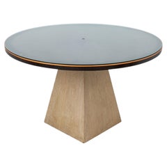 Tavolo da pranzo moderno con piano rotondo in vetro e base trapezoidale in rovere