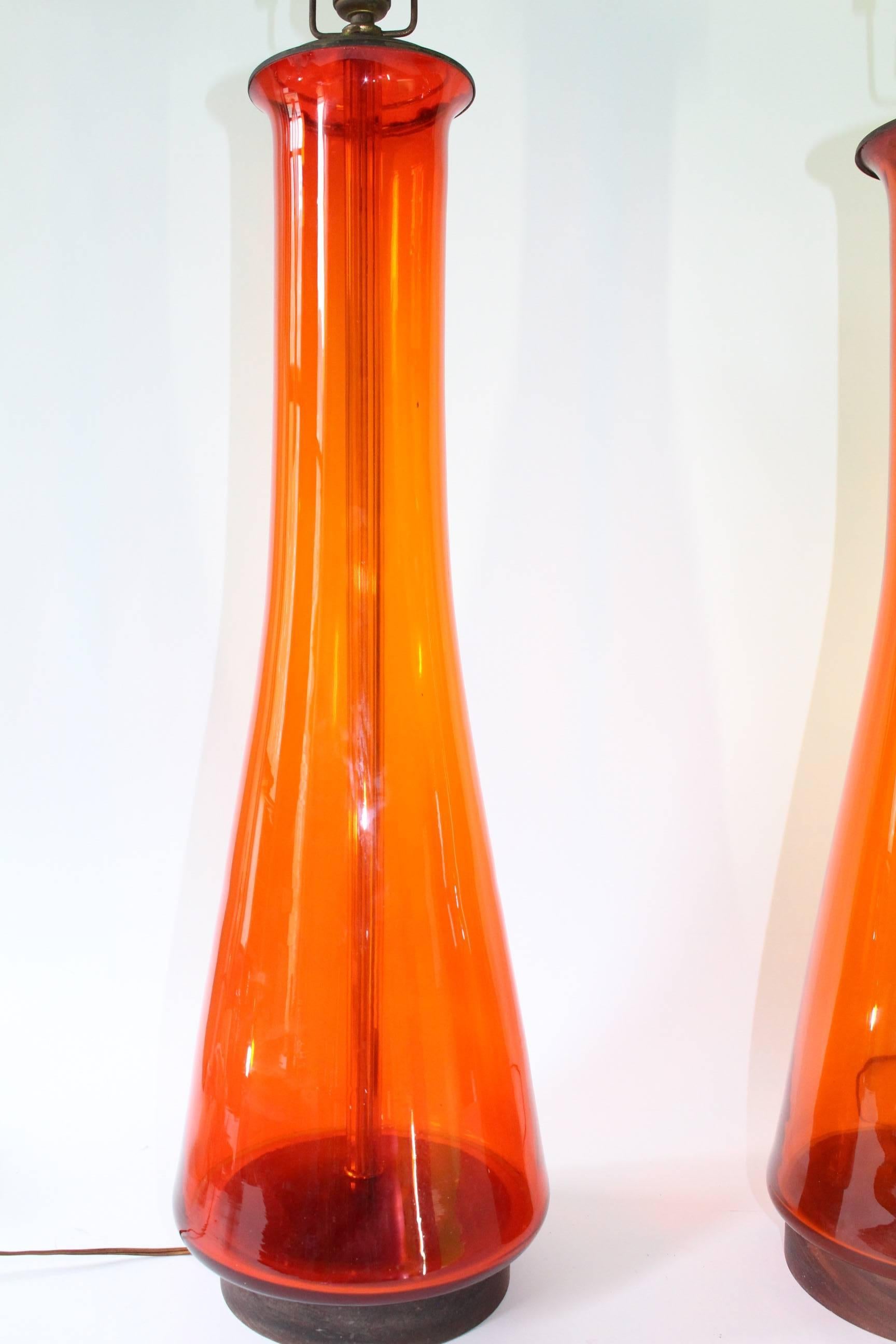 An impressive large pair of 'he' and 'she' hand-blown glass lamps by Blenko, carafe shaped, in vibrant tangerine, on round teak bases; slight variance between height, size of glass bodies (Smaller H: 26