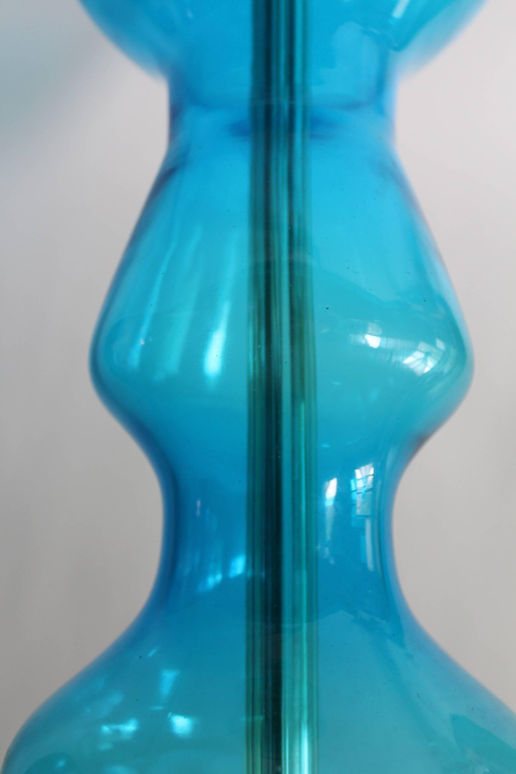 This single vintage lamp by Blenko comes in curved, handblown blue glass on teak base, harp surmounted by flame finial. Very good vintage condition, with age appropriate wear; dimensions provided reflect fully adjusted height.