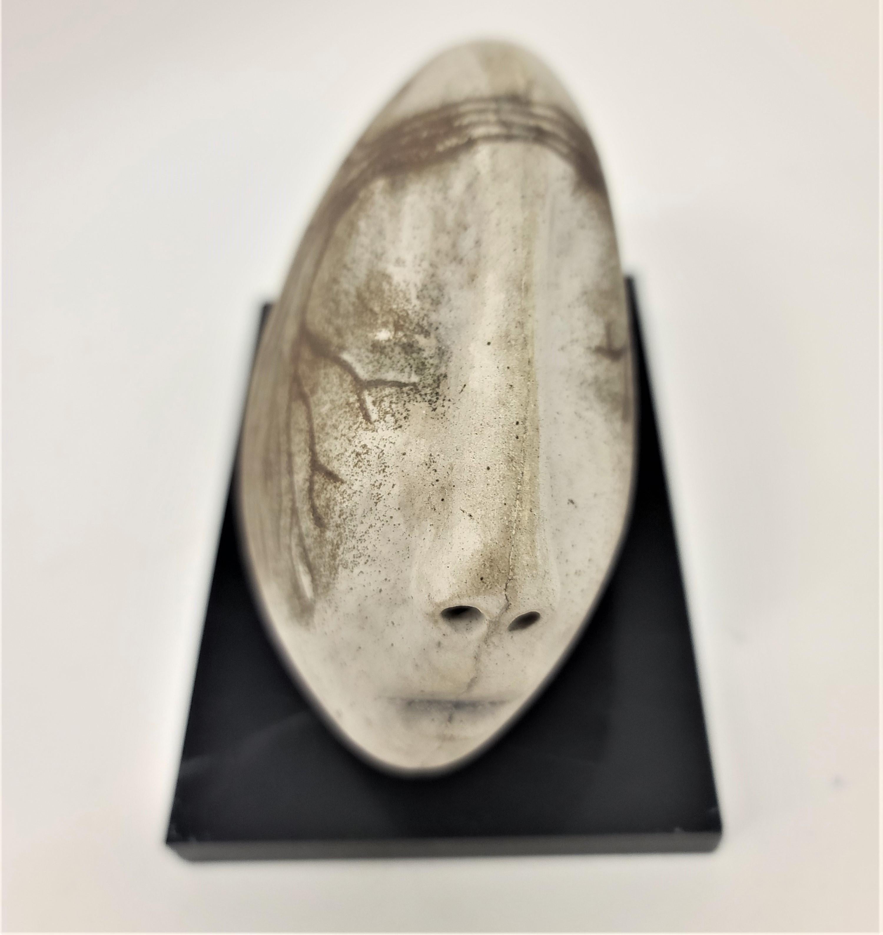 A sculpture of an abstracted head in ceramic, mounted on a black acrylic base, by an unknown artist. The human head and features have been intentionally warped into an organic stone shape, decorated with details of roots. Markings include '2'