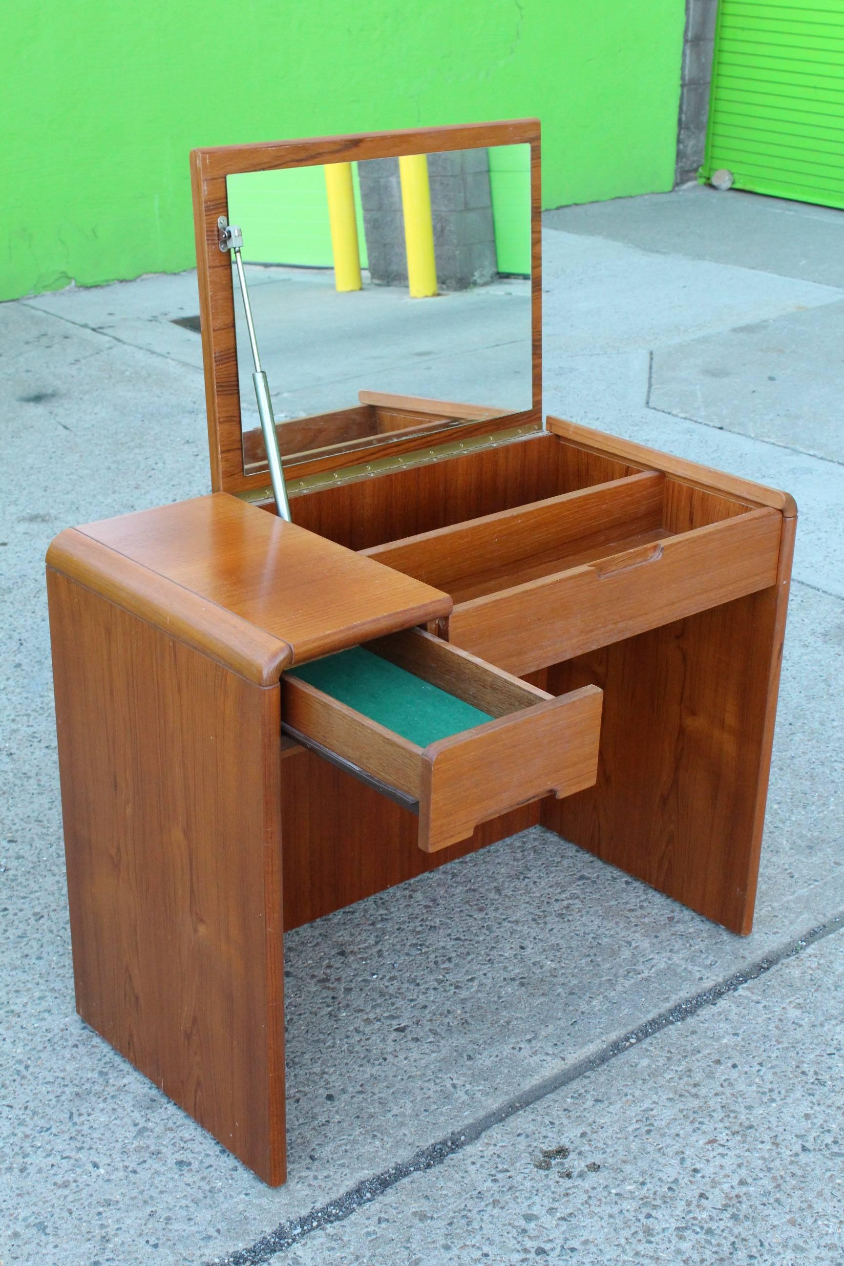 A vanity desk crafted of teakwood, manufactured circa late 20th century, with waterfall edges, including desk top, which lifts to reveal sizable mirror, over two drawers, one with ample compartment space. Very good condition, consistent with age and
