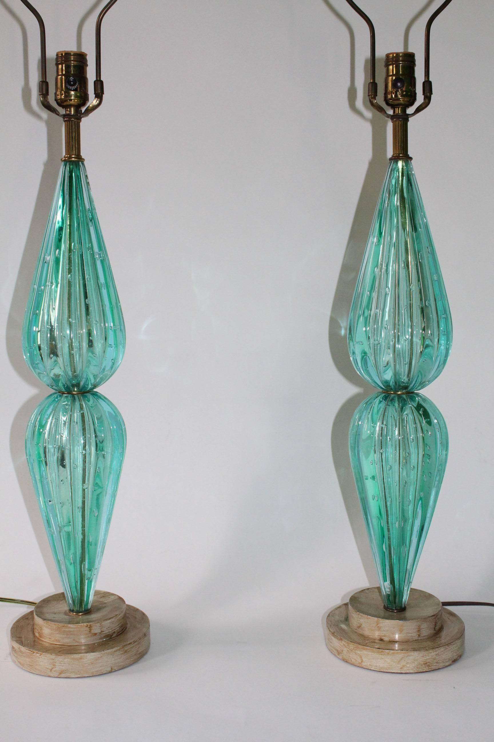 A pair of vintage Murano glass table lamps, each with single sockets over ribbed and waisted aquamarine colored bodies with 'bullicante' controlled bubbles, on circular stepped bases, with original brushed gilt paint. The lamps remain in very good