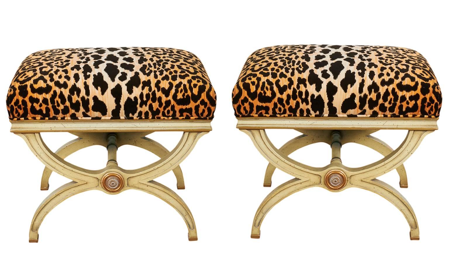A pair of Hollywood Regency style Curule benches, manufactured in the United States, circa 1940s, seats with leopard print velvet upholstery, raised on painted wood bases, accented with gold leaf. The benches are in excellent vintage condition,
