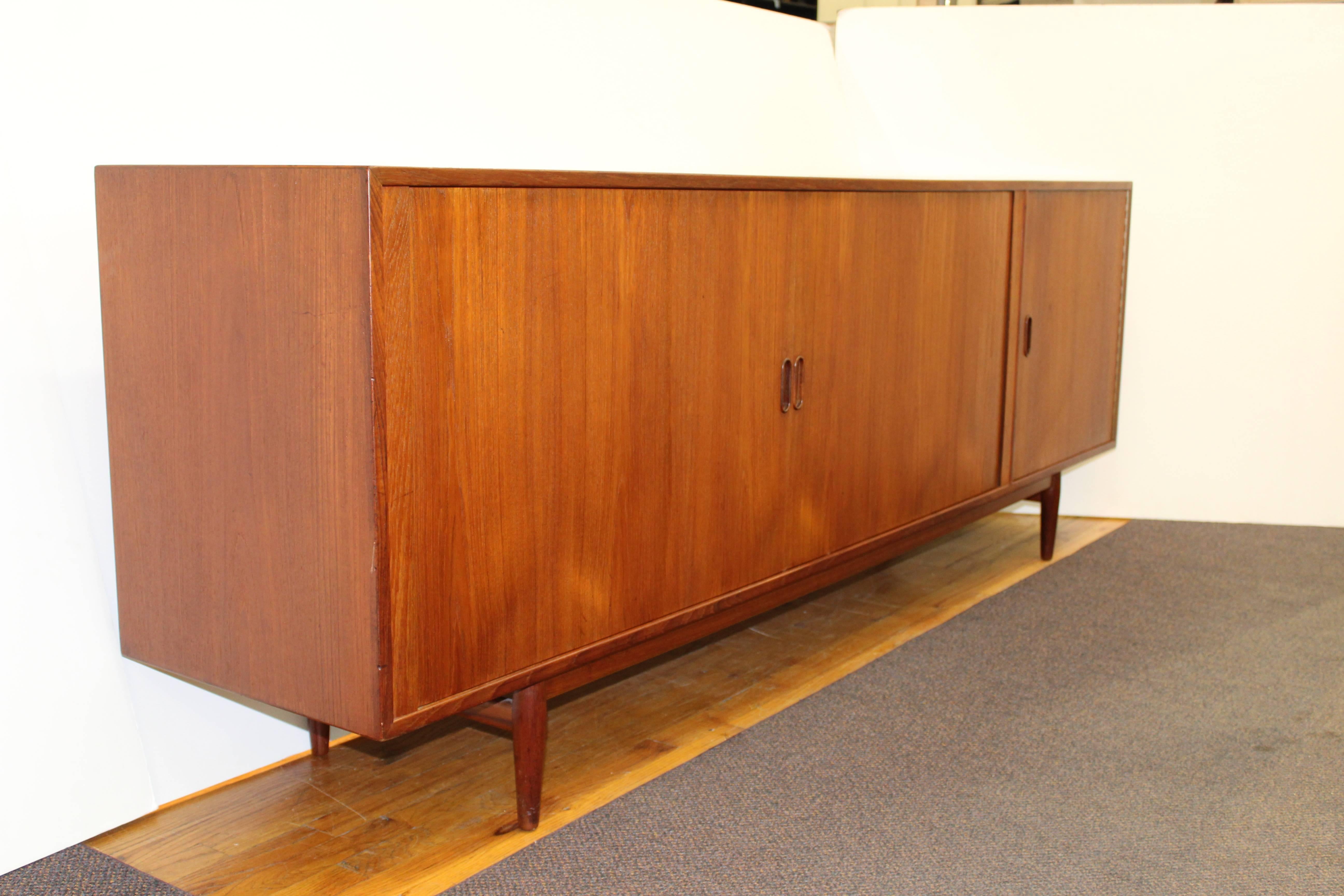 A Mid-Century credenza by Arne Vodder for Sibast in rich teak featuring two roll-front doors as well as a swing door on the right side of the middle panel. This credenza is in good vintage condition and has wear consistent with age and use.
 