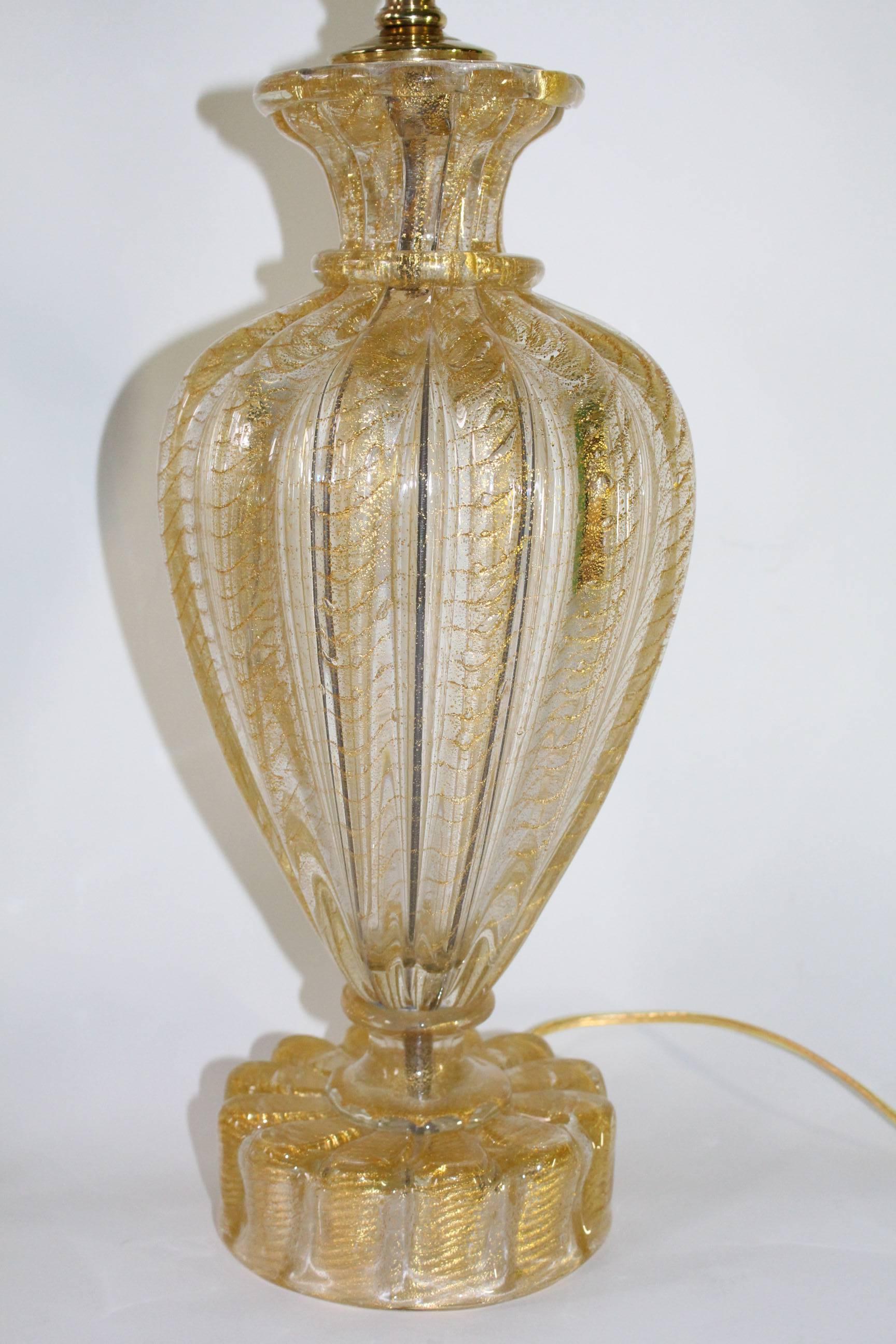 A pair of Mid-Century Murano glass lamps with gold flakes, bulb-shaped bodies and floral-shaped bases. Each lamp has a new cord, new hardware, and features a three-way switch. In very good condition. Listed height is to the top of the finial,