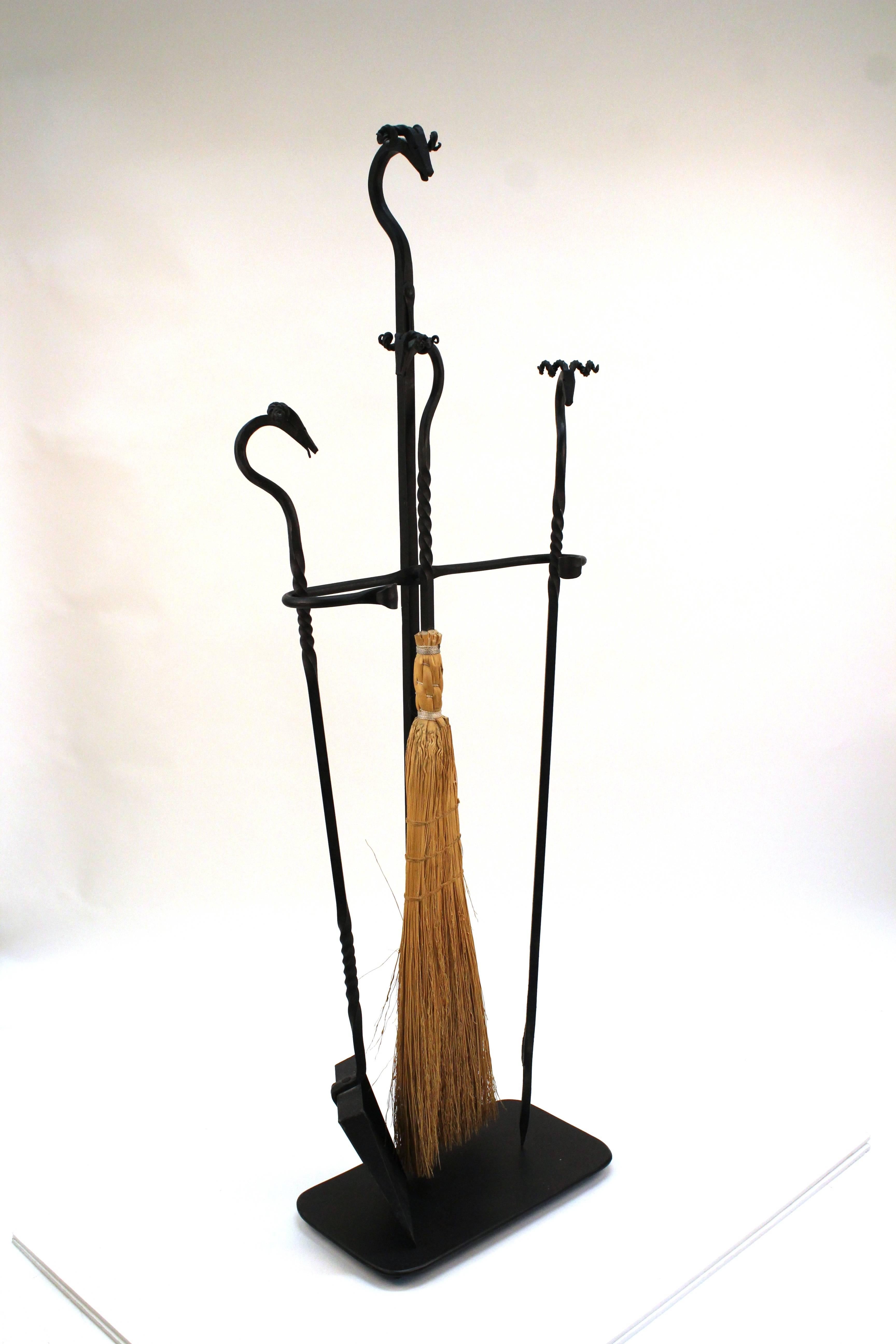 A set of fireplace tools crafted in wrought iron. The stand and tools each have a ram's head handle. Some wear due to age and use, in good condition.