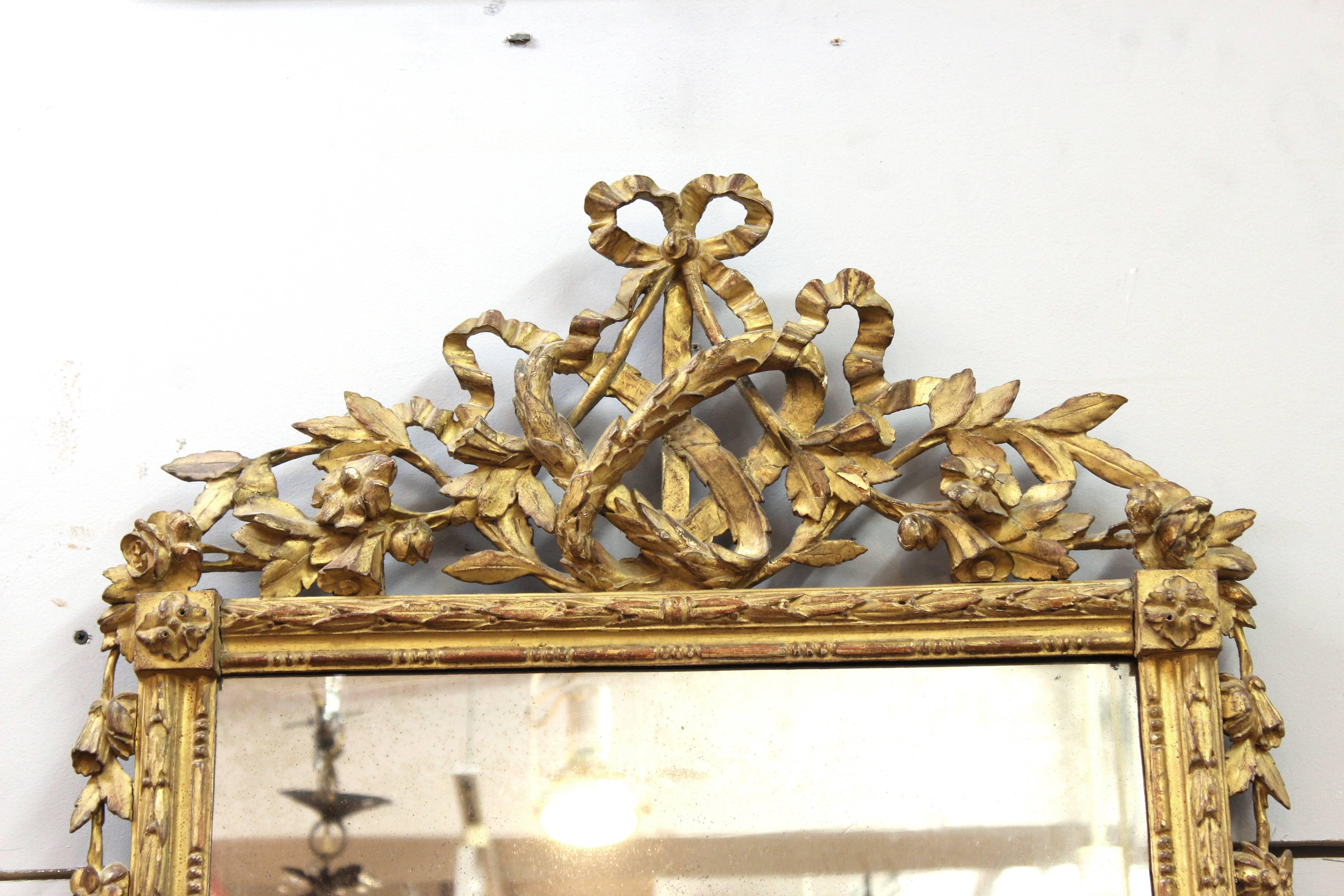 A Louis XVI or Marie Antoinette style mirror. The mirror is made up of two panels which are placed in a giltwood frame. The wooden frame is styled with garlands of flowers and ribbons. Wear appropriate to age and use including minor losses to the