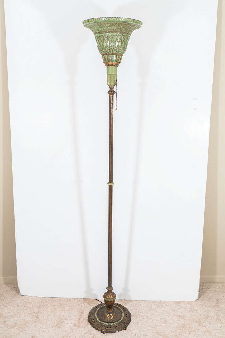 An vintage Art Nouveau torchiere floor lamp, produced circa 1910, with the original glass shade in green, etched, painted and inset into a gilt bronze frame, above a reeded brass stem on a cast brass circular base, stylistically painted and detailed