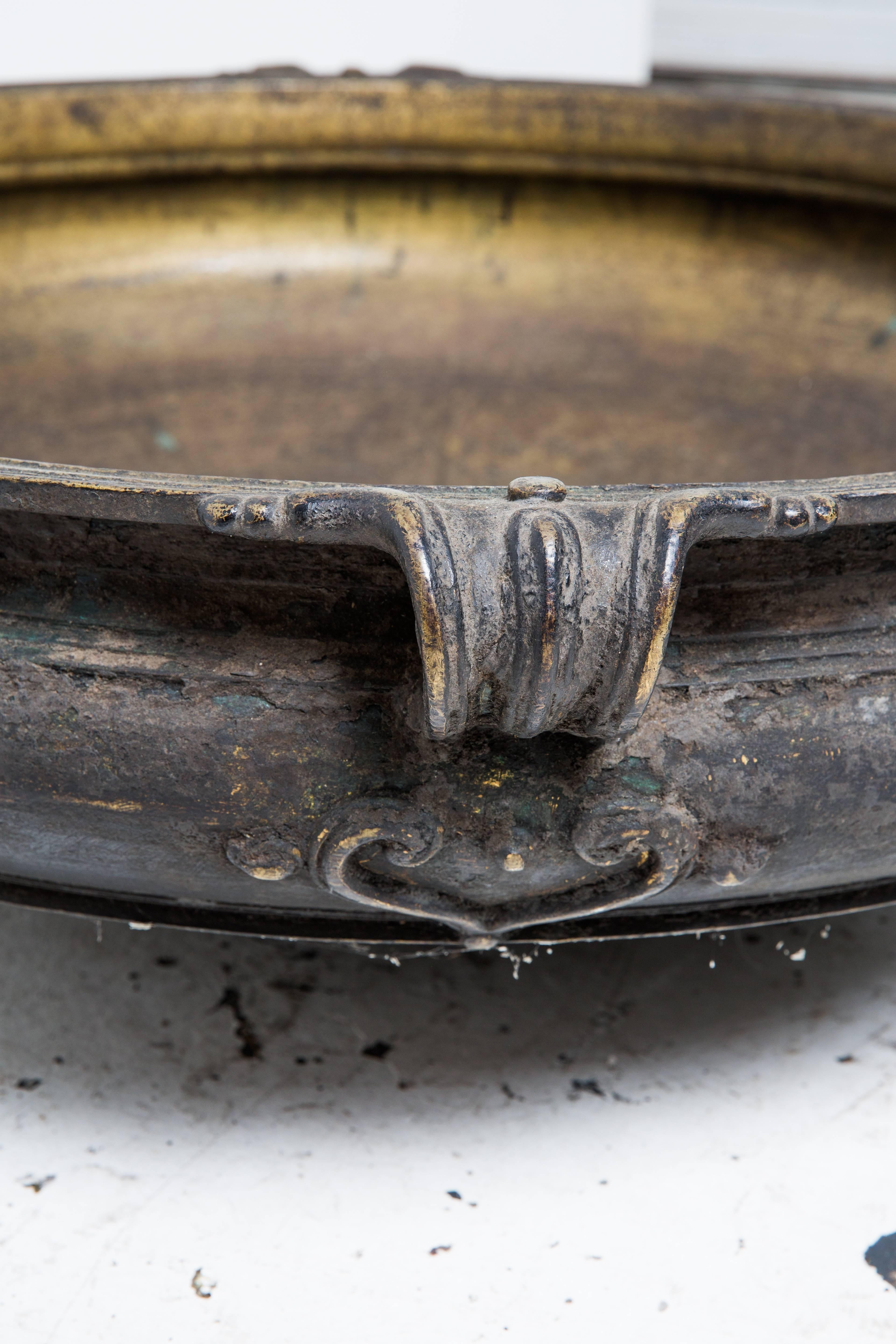 Cast brass cooking pot from southern India known locally as an urli. Pots were placed directly on a fire and large meals were prepared for special events. Wooden poles were inserted into the metal loops on the sides of the urlis to carry the heavy