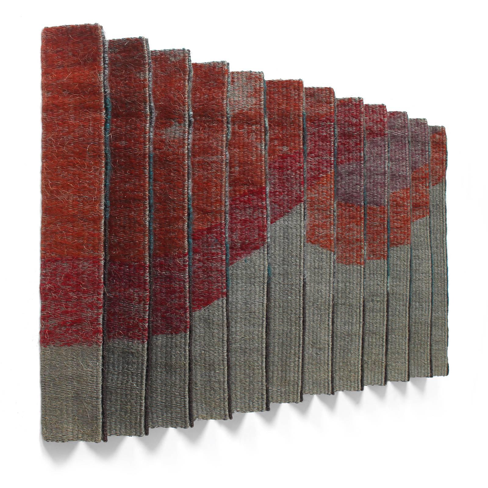 A unique wall hanging fashioned of conjoined and pleated hand woven wool panels in abstracted patterns in tones of black, gray and red.