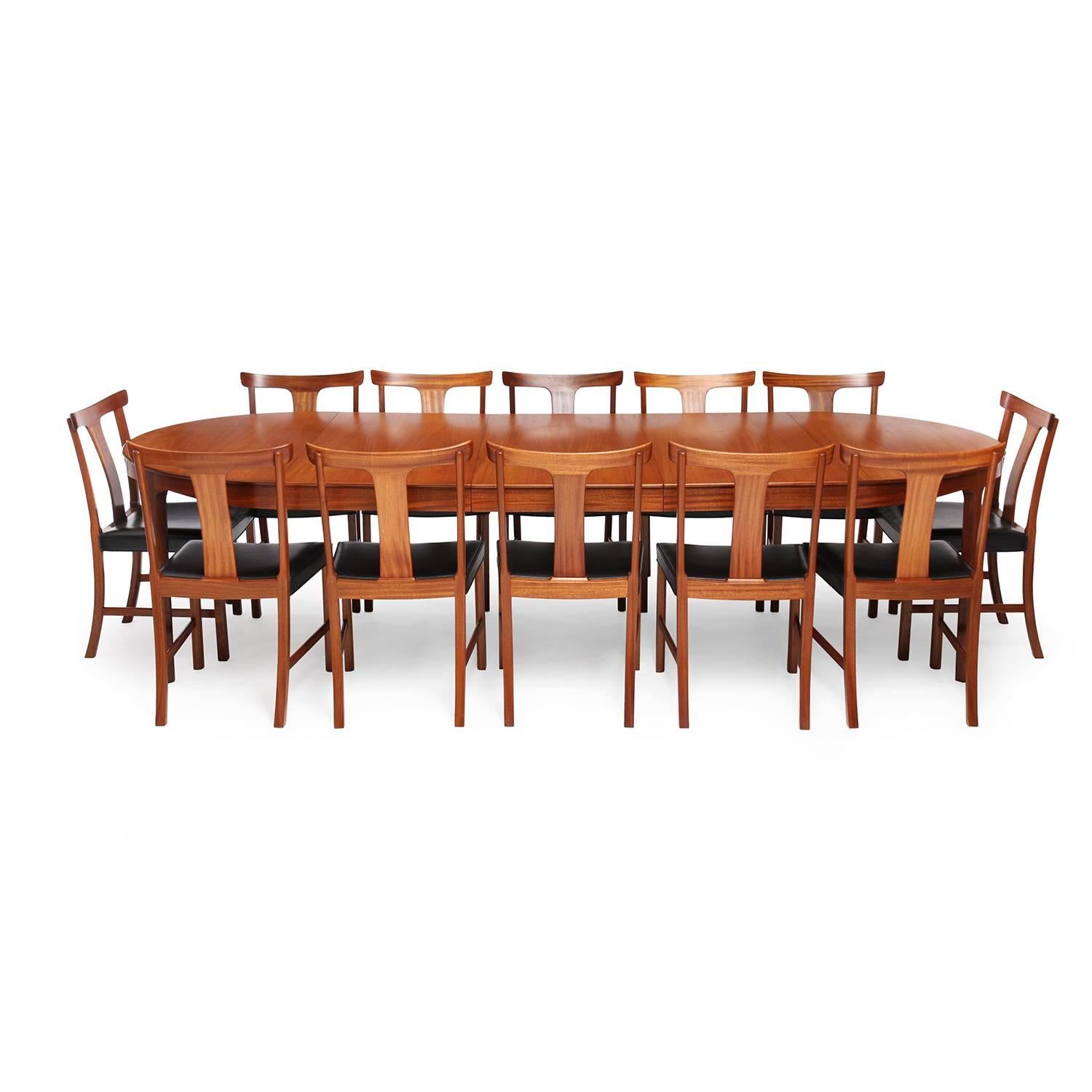 A spare, sculptural and finely proportioned expandable oval dining table in rich mahogany having a subtly scalloped apron and carved tapering legs