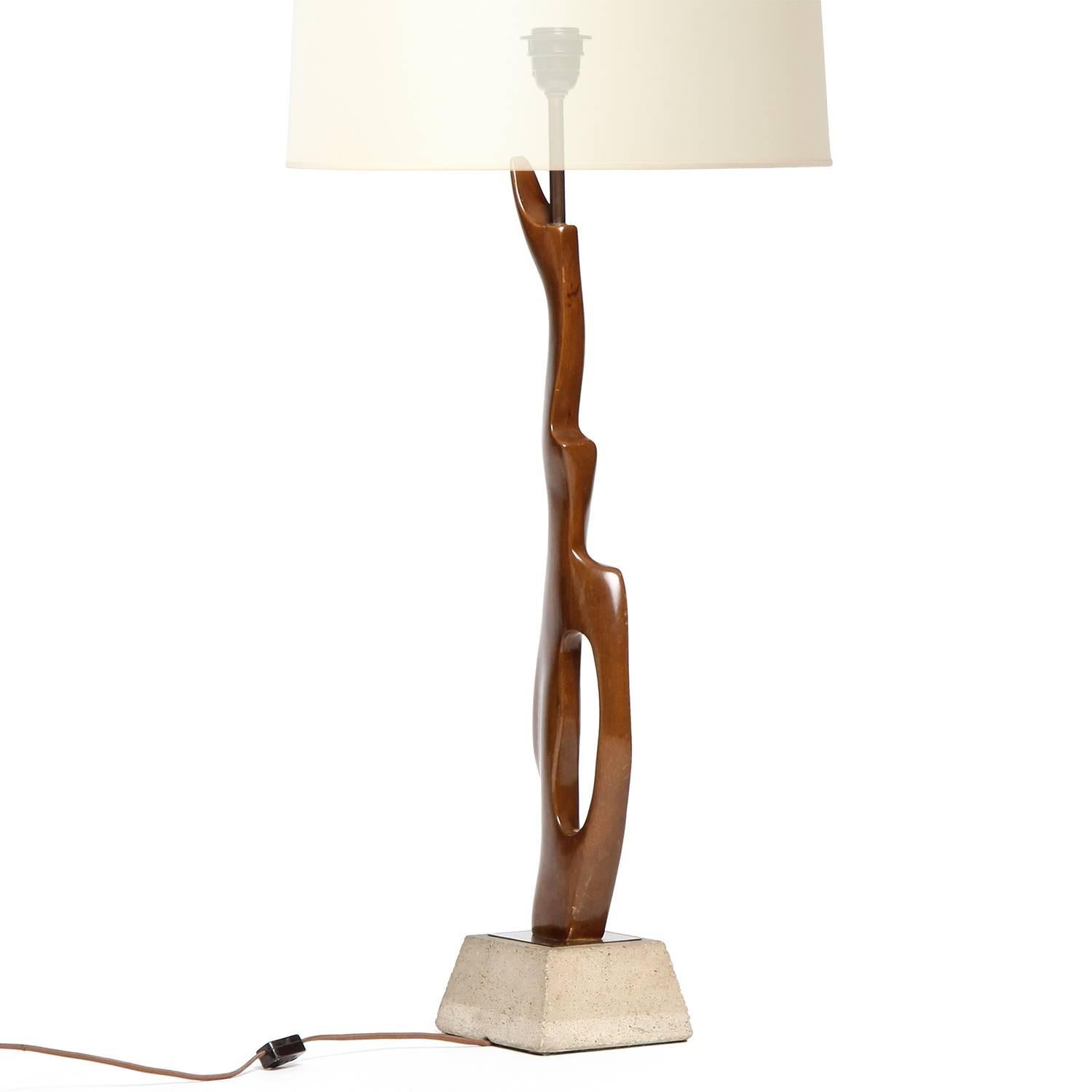 A tall and expressive biomorphic table lamp carved from a single piece of mahogany and mounted on a trapezoidal concrete base.