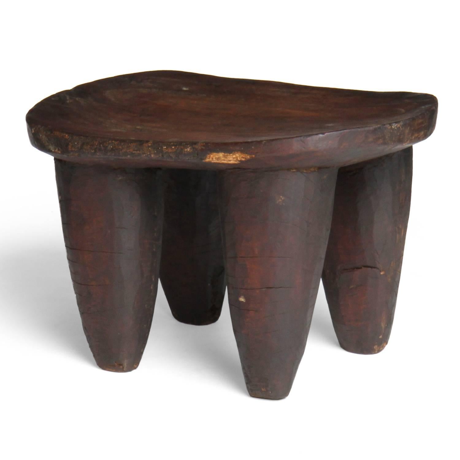 A diminutive and finely carved four-legged tribal stool crafted from a single piece of dense hardwood.