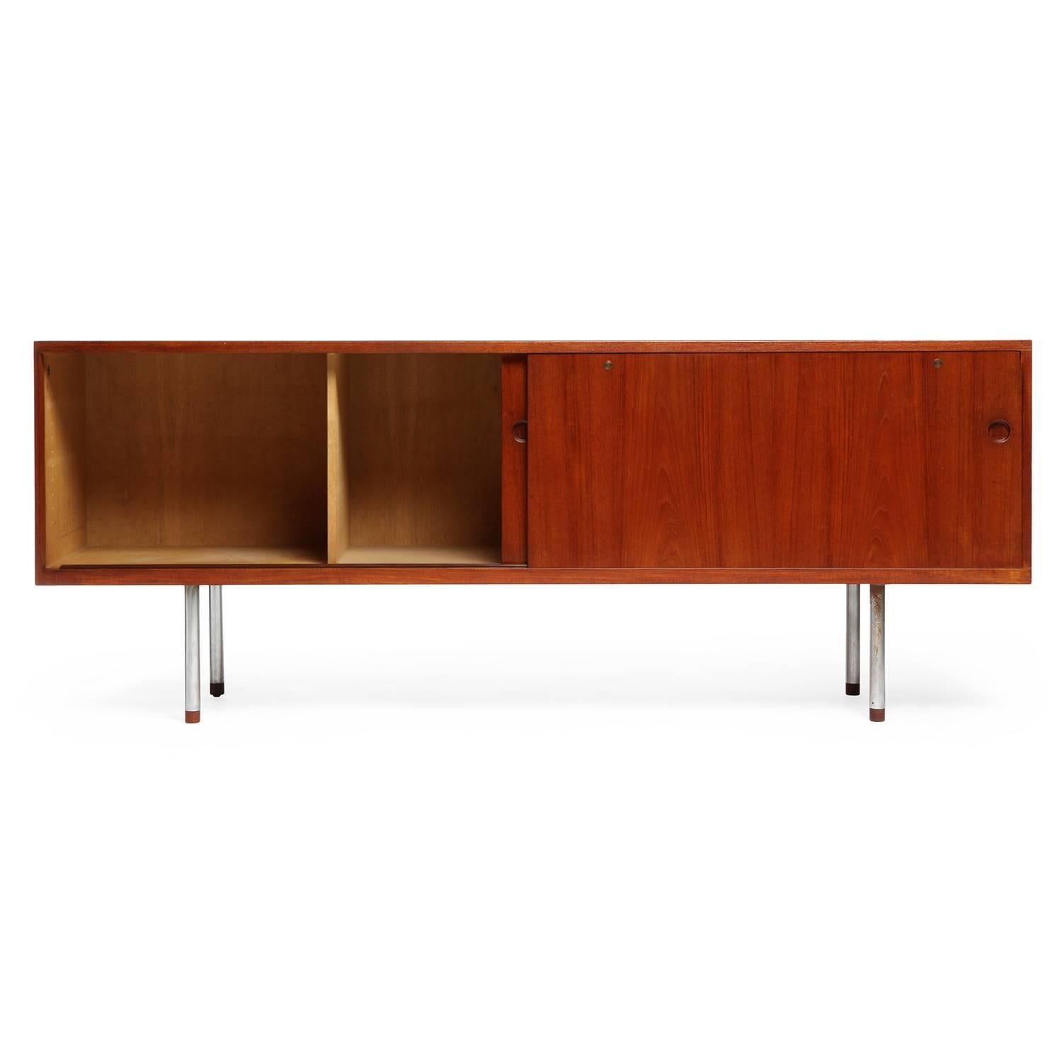 A fine and long credenza of spare rectilinear form having sliding doors with recessed pulls, the case floating on cylindrical brushed steel wood-capped legs.