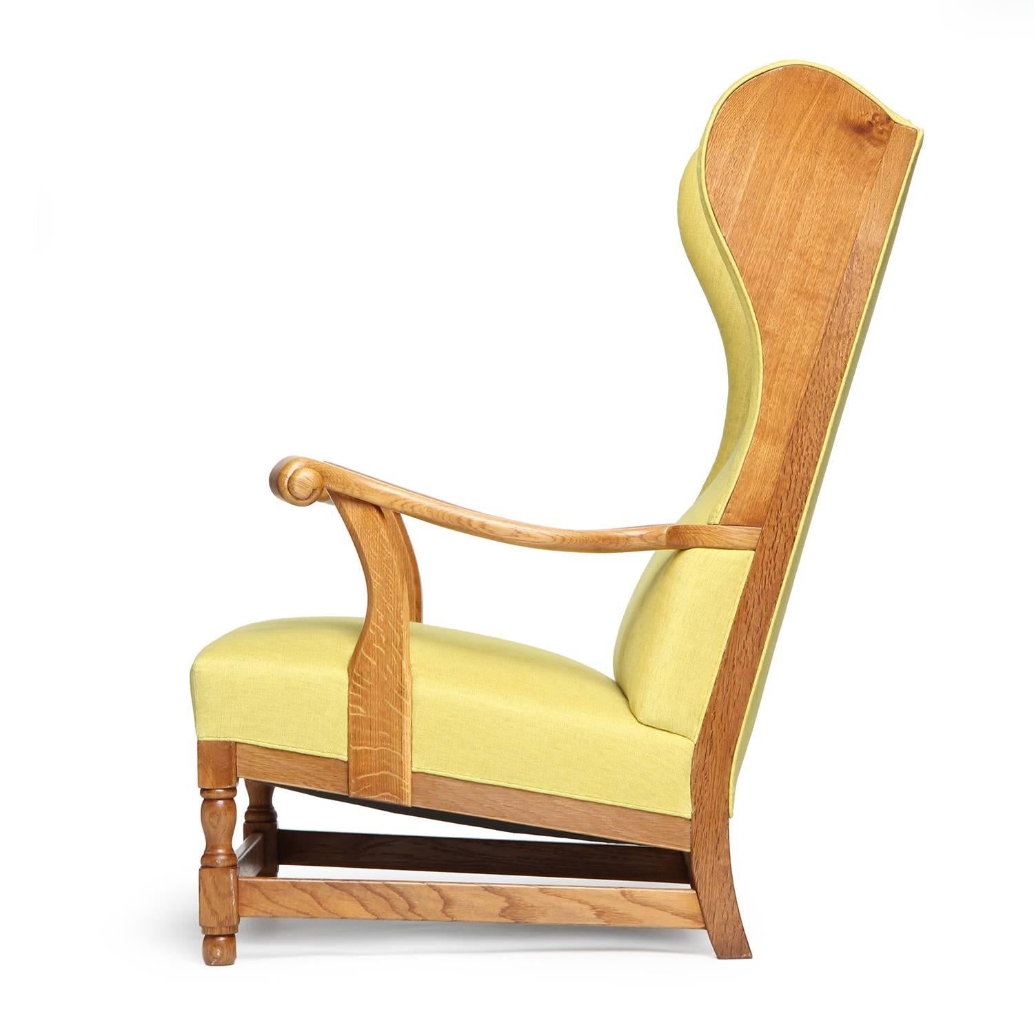A highly expressive and well scaled upholstered wingback chair having sculpted knuckled arms and an exposed oak wood frame.